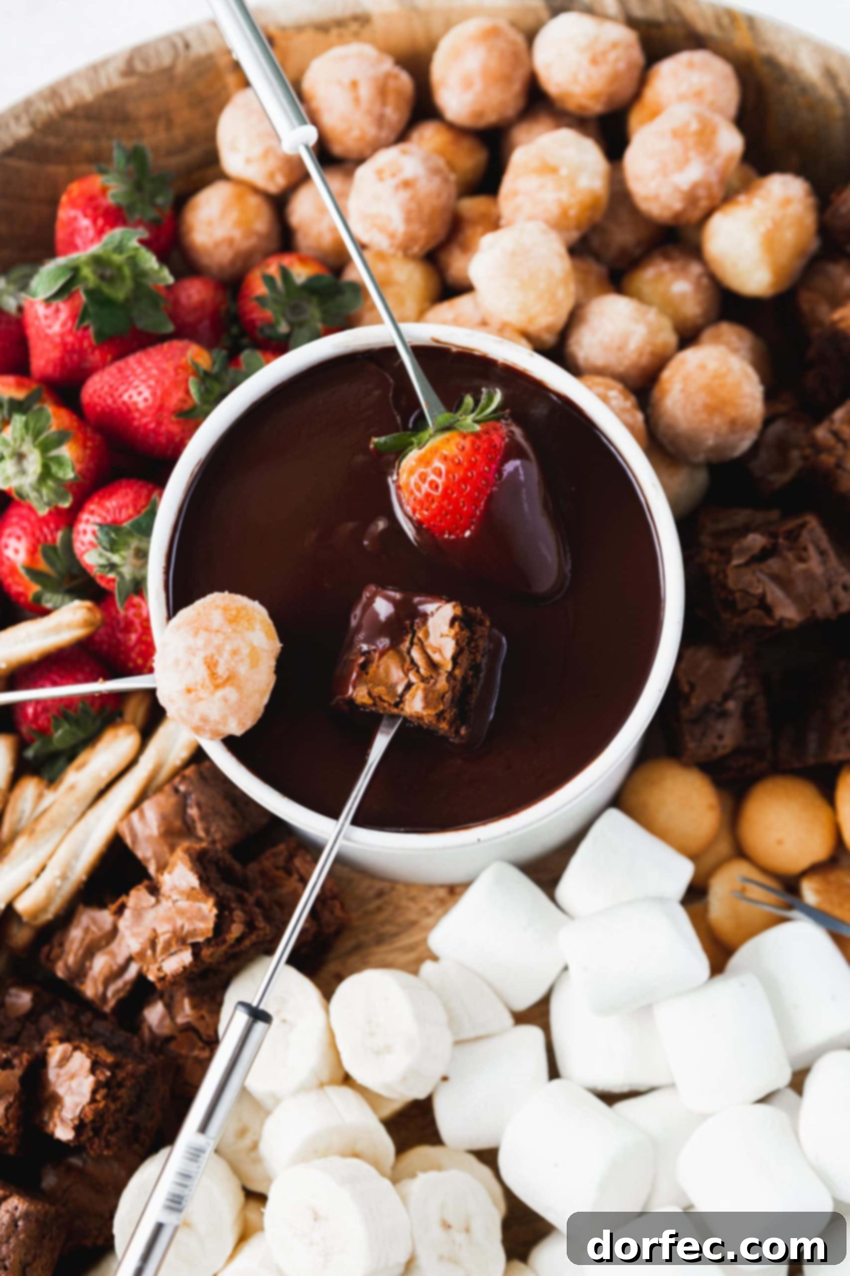 Fondue Party Spread A bowl of chocolate fondue in which a strawberry, brownie and donut hole are being dipped. There are strawberries, donut holes, brownies, marshmallows, and other things to dip in the chocolate surrounding the bowl.