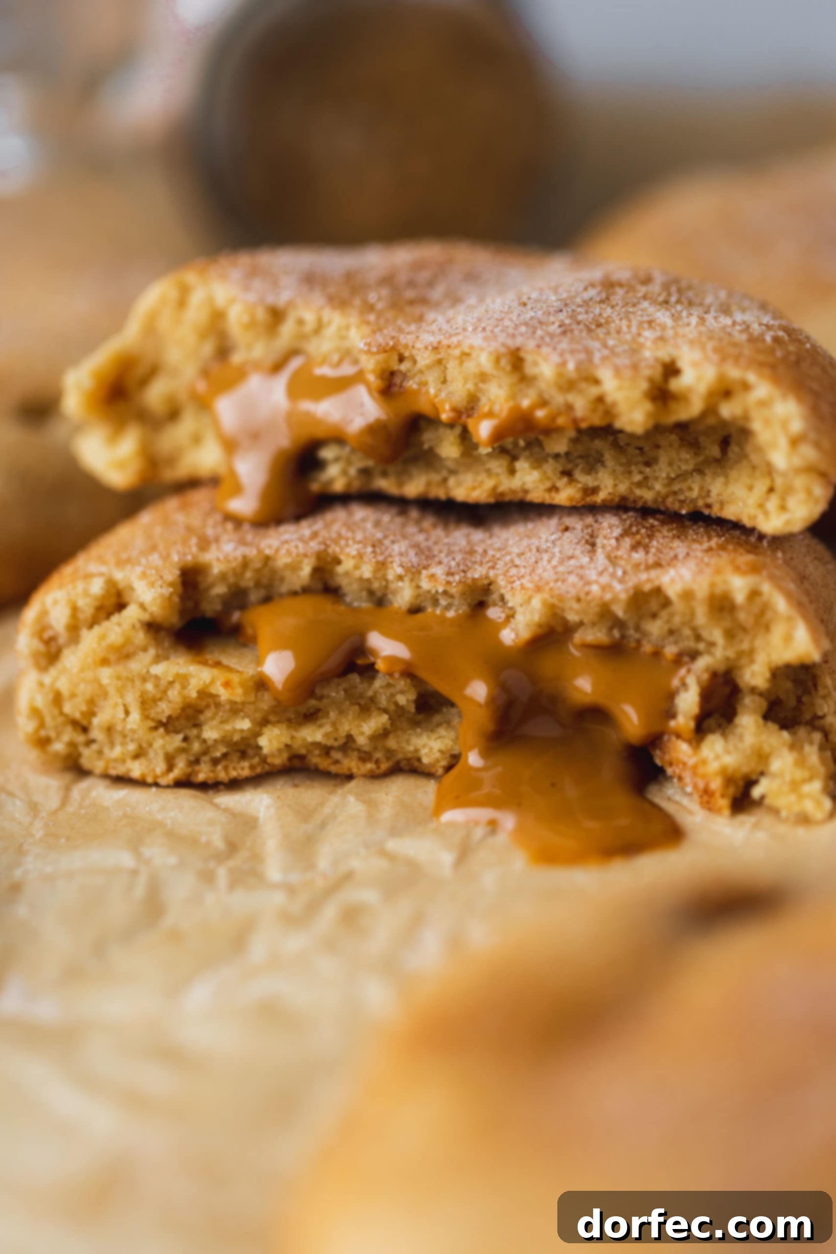 A biscoff stuffed snickerdoodle broken in half and the halves are stacked on top of each other. The biscoff center is oozing out onto the parchment paper.