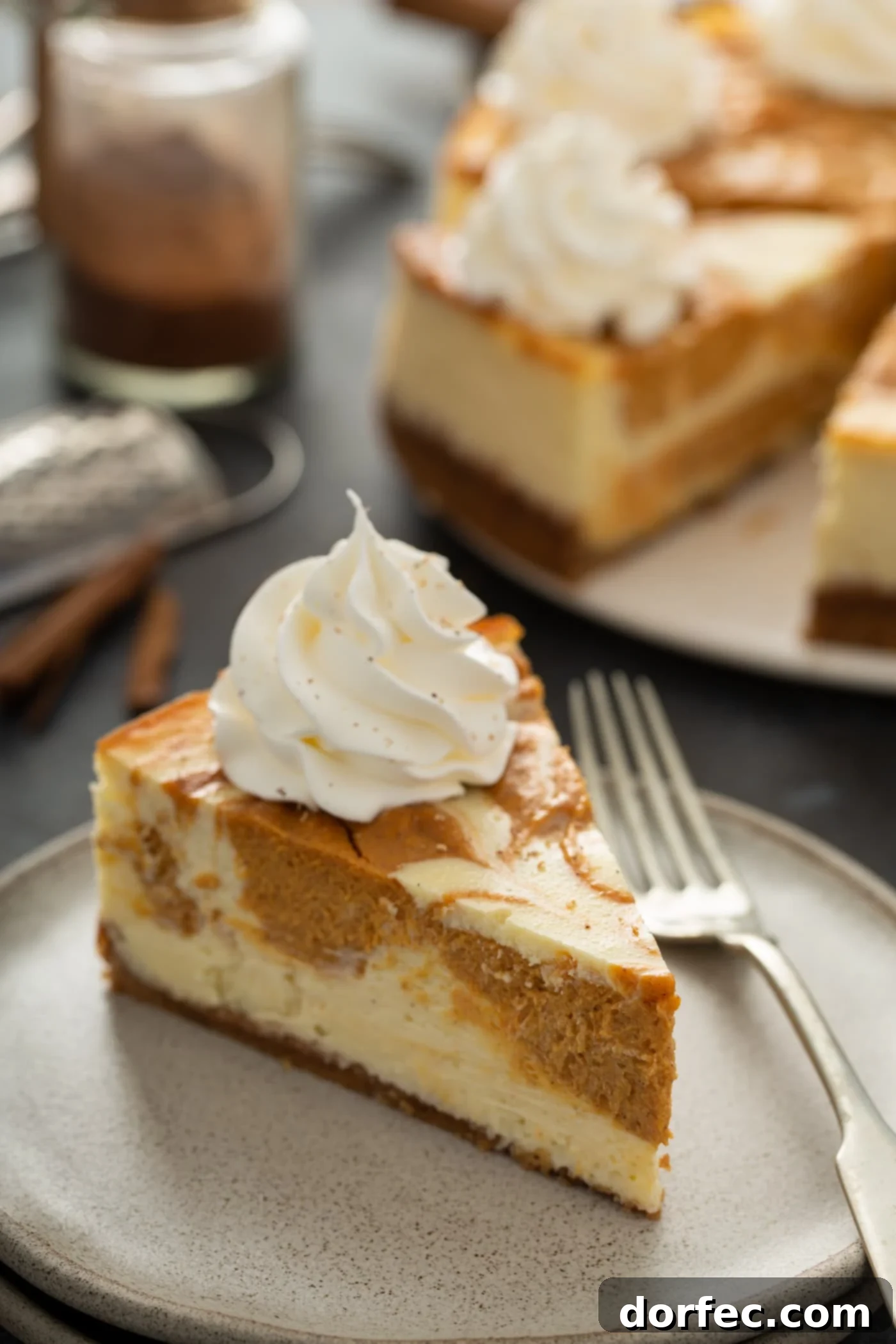 A slice of swirled pumpkin cheesecake on a plate with a fork. The rest of the cheesecake is in the background.