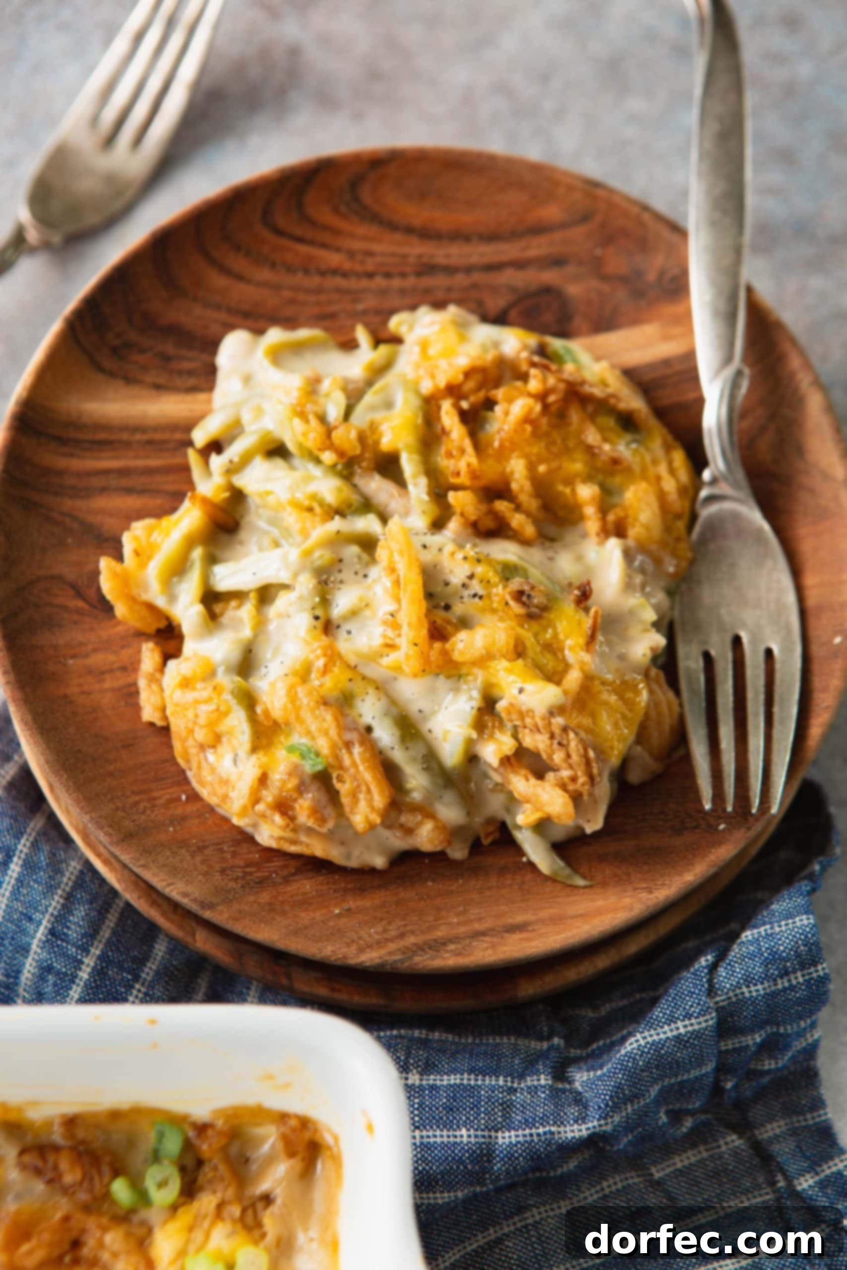 A serving of green bean casserole on a wooden plate with a fork next to it. You can see the green beans mixed in with the sauce and topped with golden brown French fried onions.