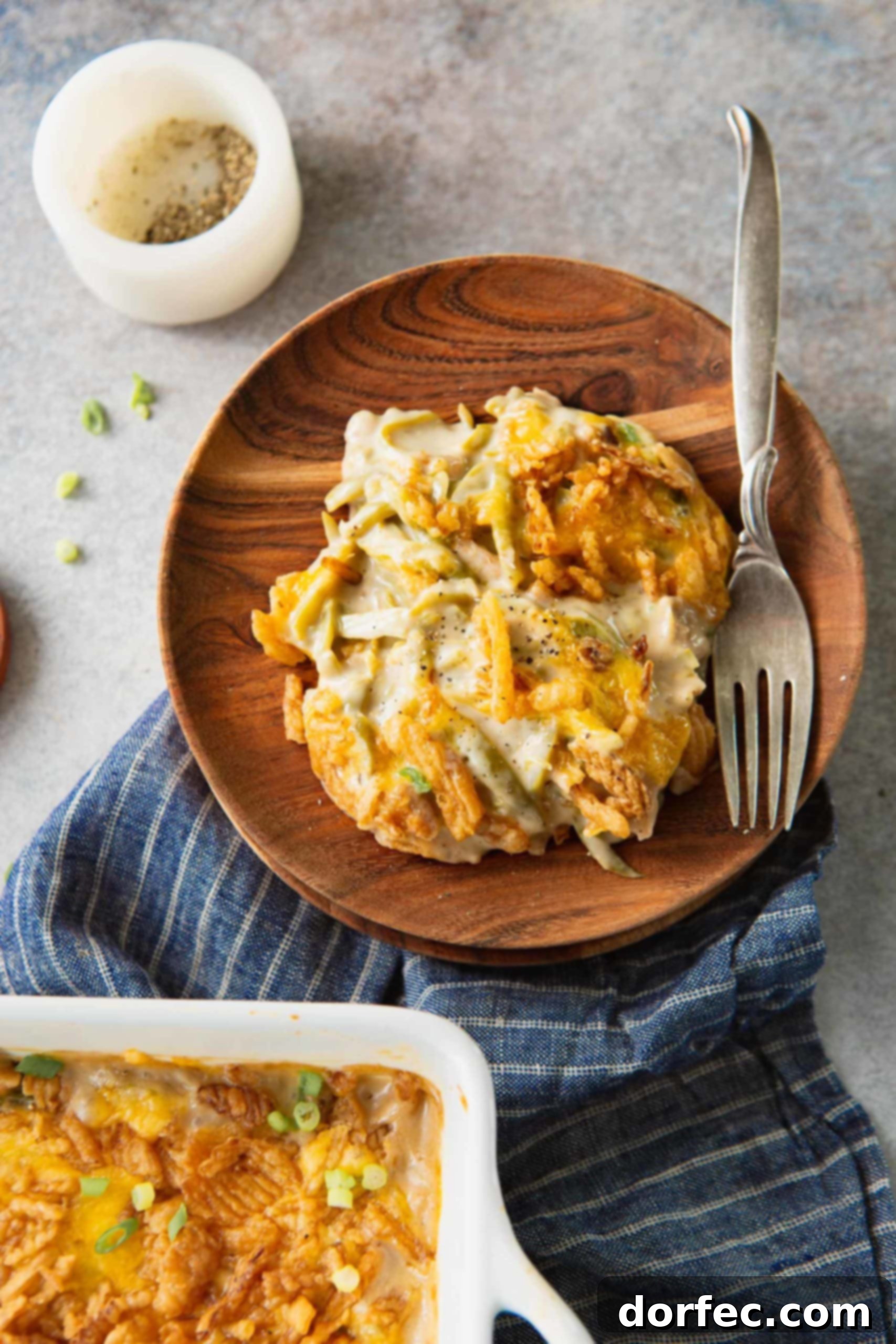 A serving of green bean casserole on a wooden plate. There is a fork next to the serving. You can see the green beans in the creamy sauce and the golden brown French fried onions on top.