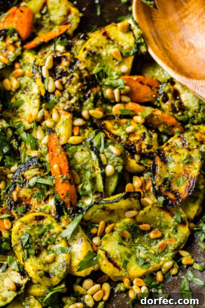 A colorful medley of grilled vegetables, lightly charred, and tossed with fresh vibrant pesto, served on a white plate.