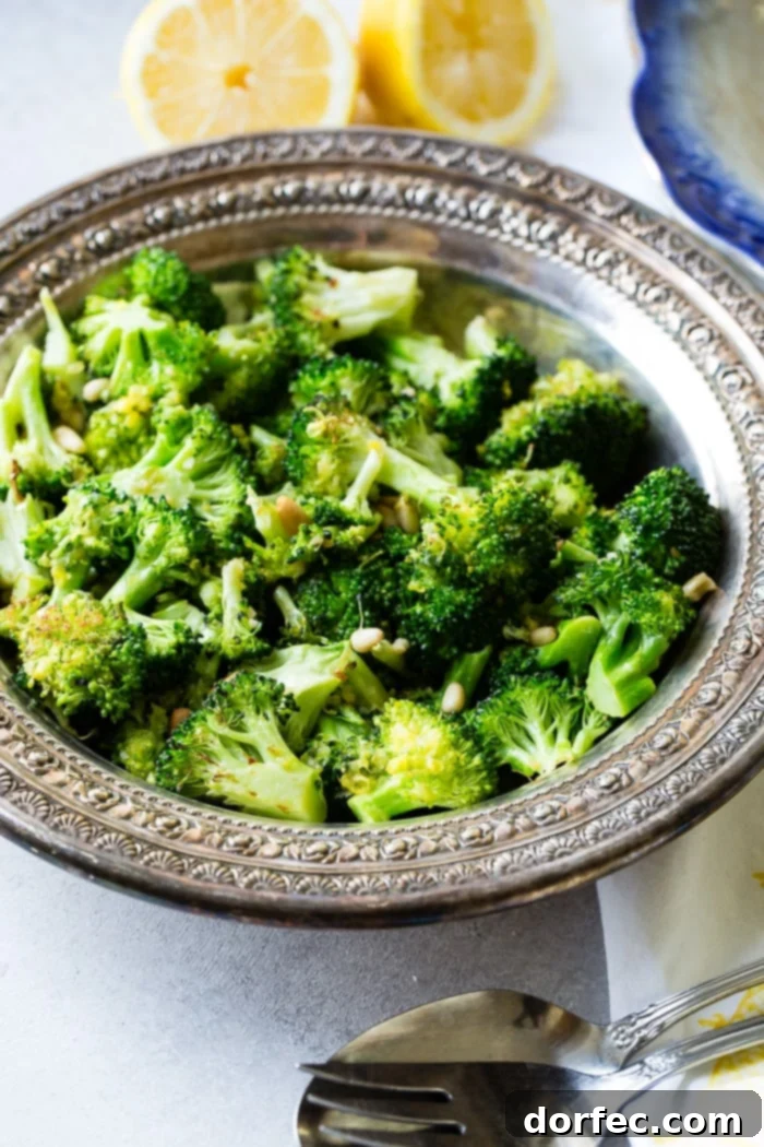 A vintage silver bowl filled with lemon roasted broccoli, garnished with pine nuts and grated parmesan cheese.