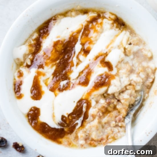A white bowl of lightened up cinnamon roll oatmeal with a swirl of butter and brown sugar mixture and a cream cheese glaze, with a vintage spoon tucked under.