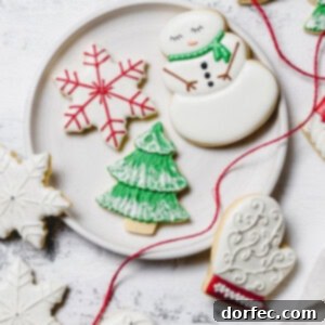 A plate with Christmas sugar cookies decorated with royal icing. There is a snowman with a green scarf, a white mitten with red trim, a green tree with white snow accents, and a white star with red accents. A red ribbon is draped over the edge of the plate.