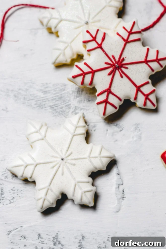 Festive Glaze for Holiday Cookies 3 Close-up of elegant Christmas sugar cookies decorated with intricate royal icing designs, featuring two delicate snowflakes, one with pristine white accents and another with festive red detailing.