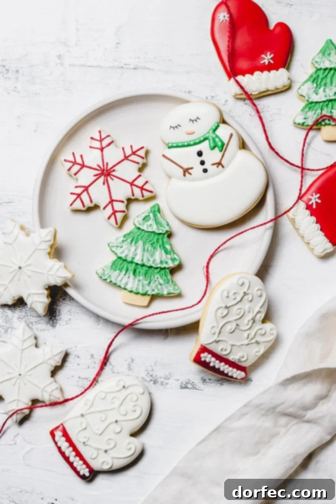 Festive Glaze for Holiday Cookies 10 A charming plate filled with festive Christmas sugar cookies, all beautifully decorated with vibrant royal icing. Designs include a cheerful snowman with a green scarf, a delicate snowflake with red accents, a lush green Christmas tree dusted with white snow, a cozy white mitten with red trim, and several pristine white snowflakes.
