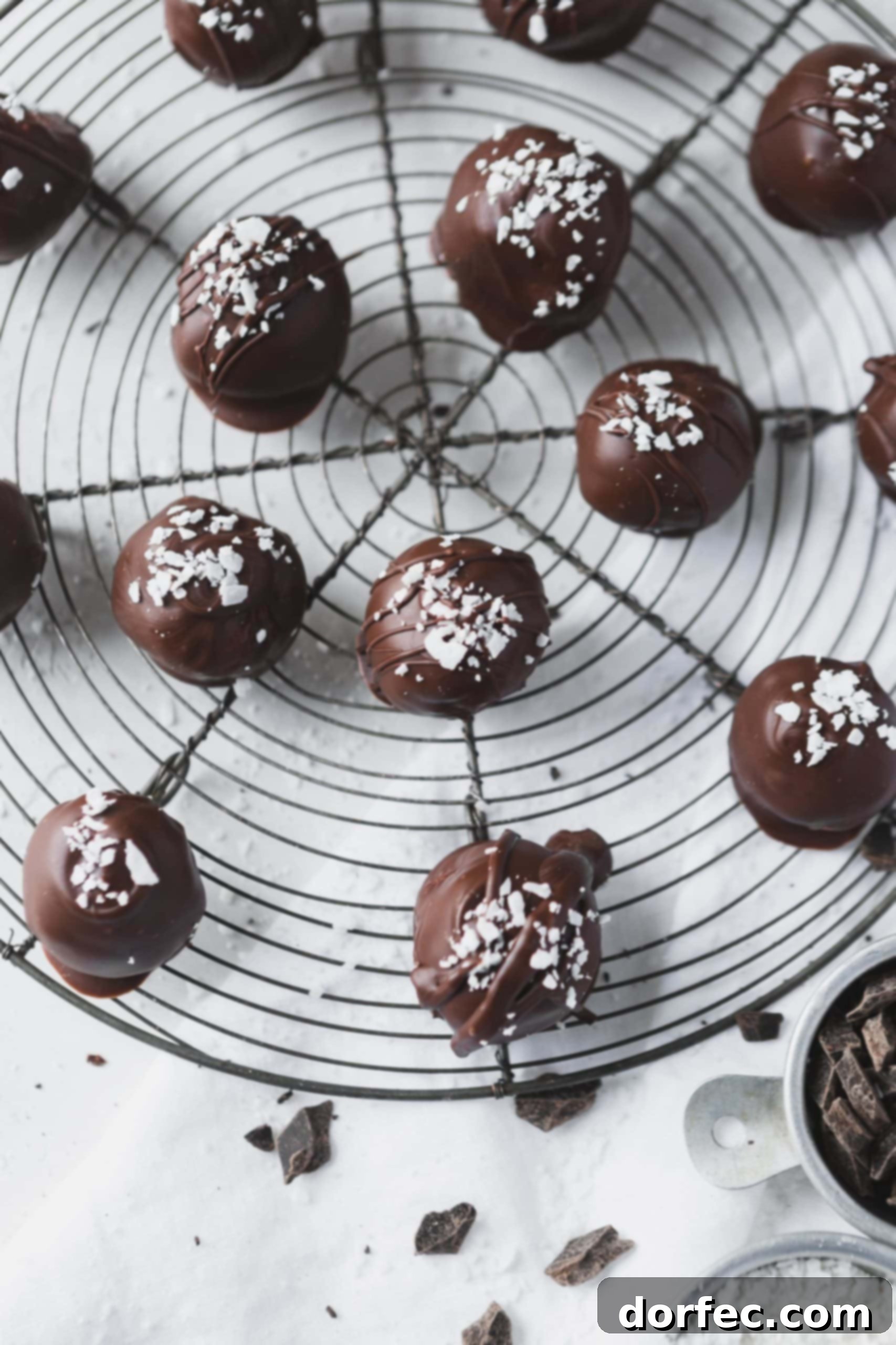 A round wire rack showcasing freshly made chocolate covered coconut balls, lightly sprinkled with coconut flakes, ready to be enjoyed.