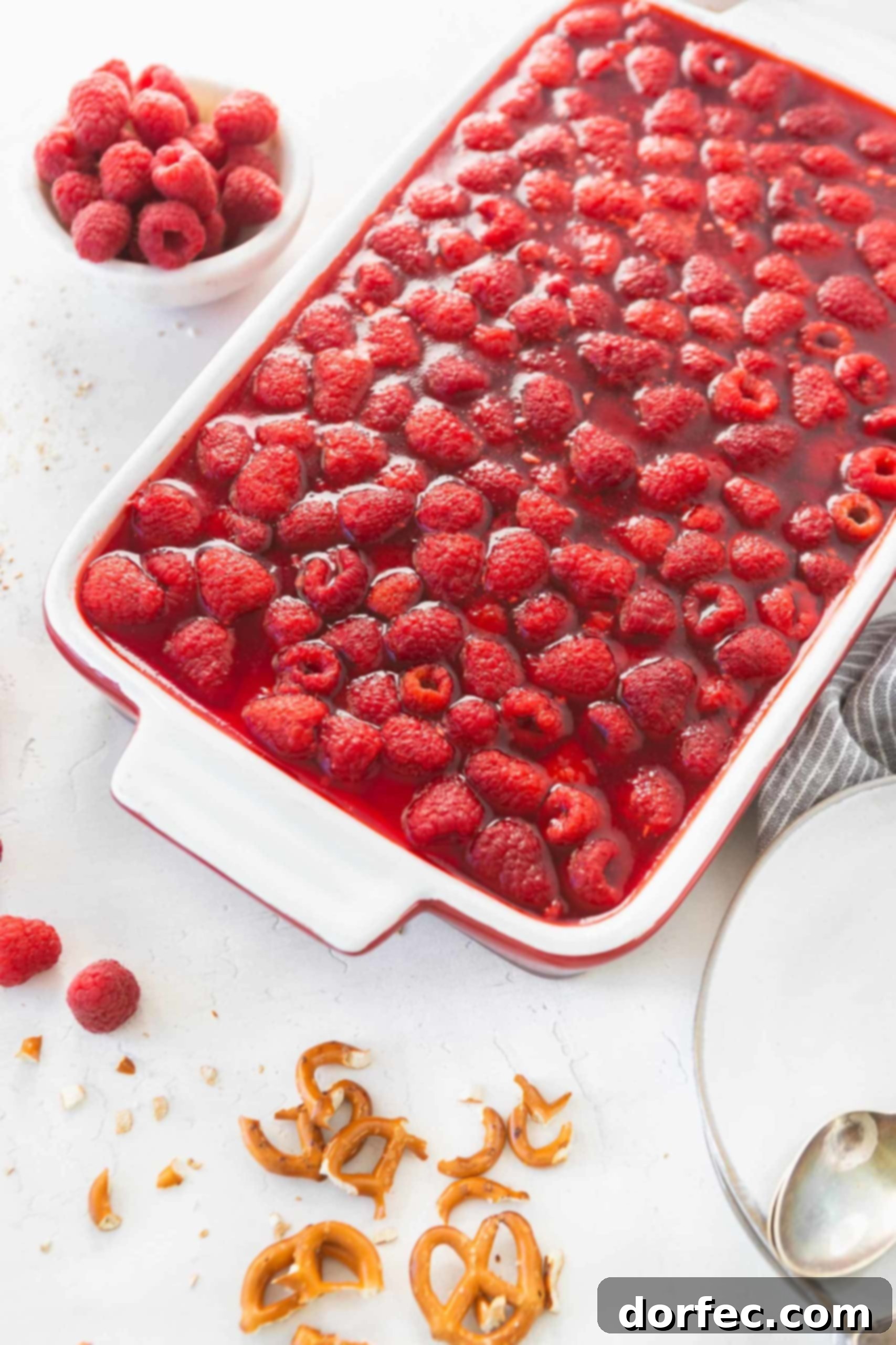 A large white casserole dish filled with Raspberry Pretzel Jello Salad, showing the thick, ruby-red jello layer bursting with fresh raspberries. The creamy layer is subtly visible beneath.
