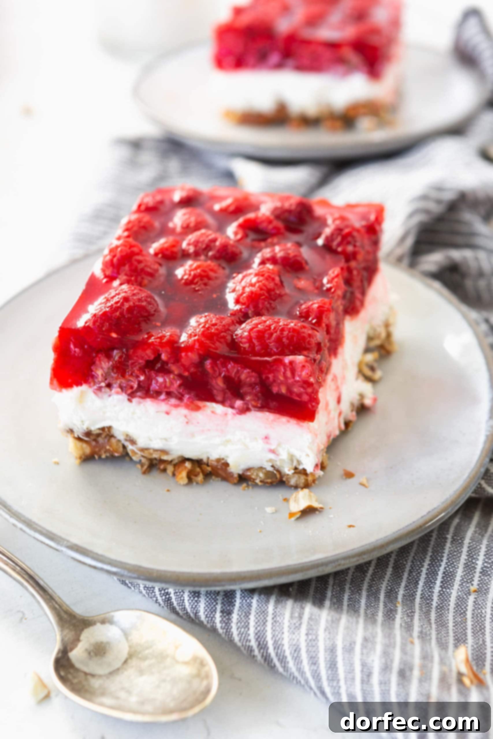 A beautifully presented serving of Raspberry Pretzel Jello Salad on a white plate, clearly displaying all three distinct layers: the golden pretzel crust, the creamy white filling, and the translucent red jello layer generously filled with fresh raspberries.