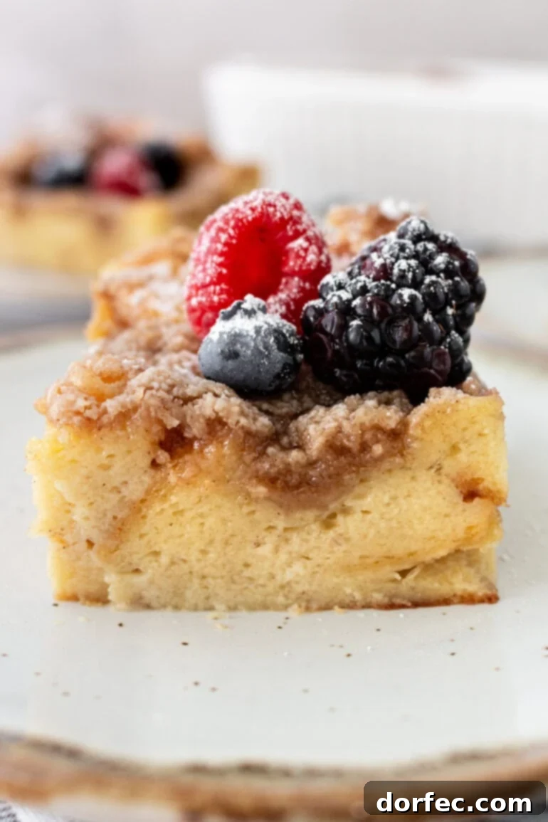 Overnight French Toast Bake 2 A delicious piece of Easy French Toast Casserole, garnished with fresh, vibrant berries and a dusting of powdered sugar, served on a pristine white plate.