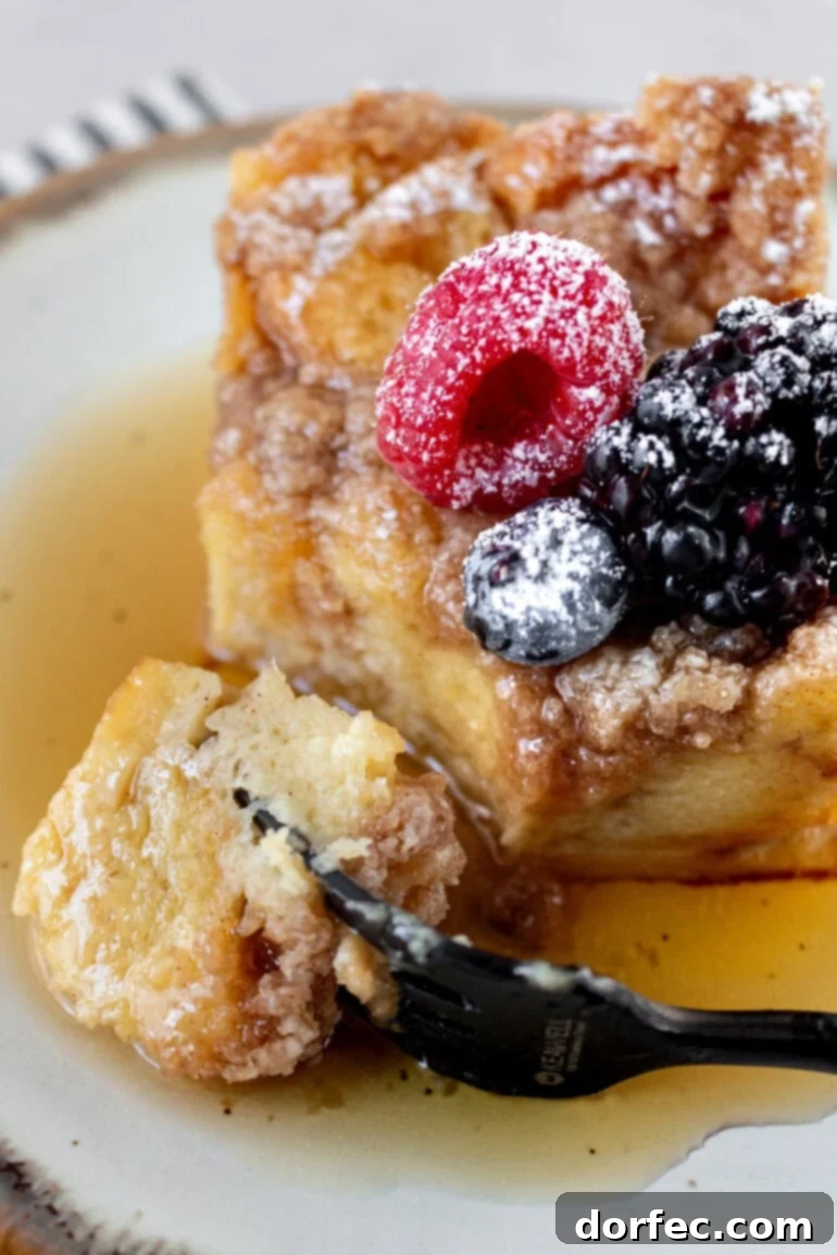 Overnight French Toast Bake 11 A fork is poised to take a bite from a fluffy piece of French toast casserole, highlighting its soft, custardy texture.
