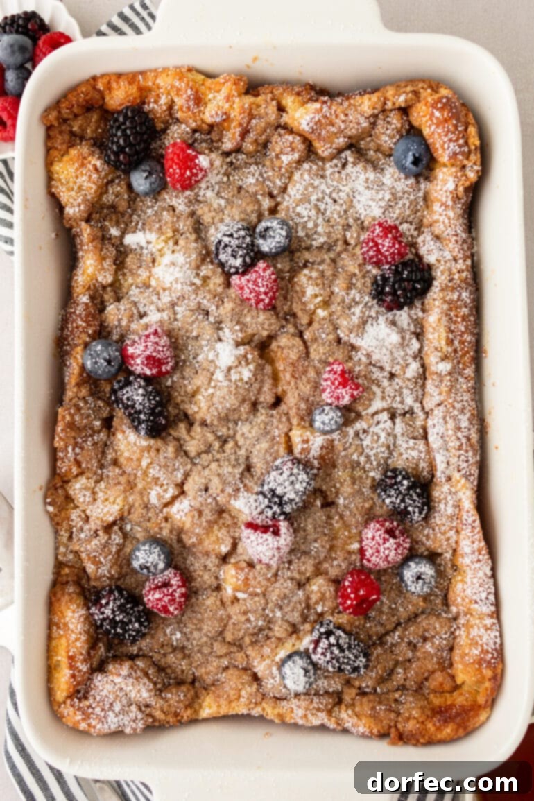 Overnight French Toast Bake 9 A golden-brown baked French toast casserole, adorned with a sweet streusel topping, a dusting of powdered sugar, and an arrangement of fresh berries, signifying a perfectly finished dish.