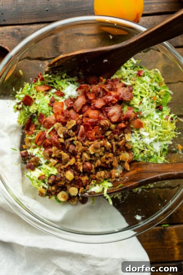 Jewel-Toned Brussels Sprouts with Pomegranate 3 A glistening glass bowl filled with vibrant pomegranate Brussels sprout salad, featuring glistening candied nuts, bright red pomegranate arils, and crispy bacon bits nestled amongst the shaved Brussels sprouts.