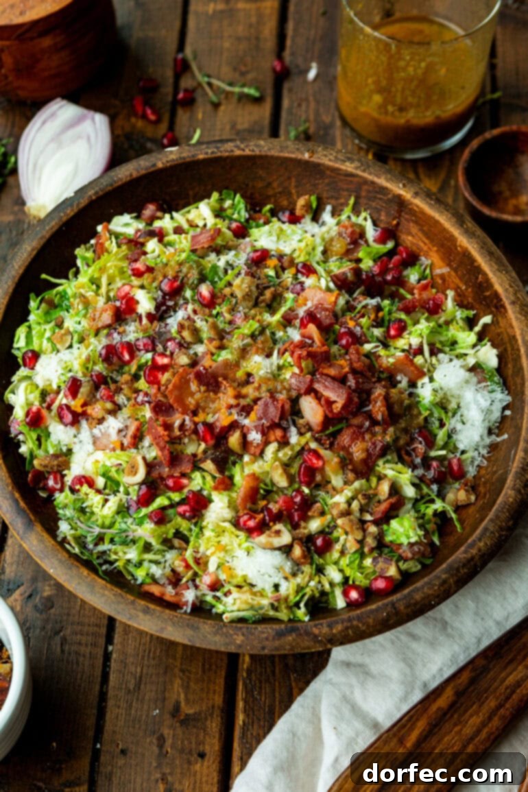 Jewel-Toned Brussels Sprouts with Pomegranate 5 A vibrant bowl of pomegranate Brussels sprout salad, brimming with shaved Brussels sprouts, crispy bacon bits, glistening pomegranate arils, and crunchy candied nuts.