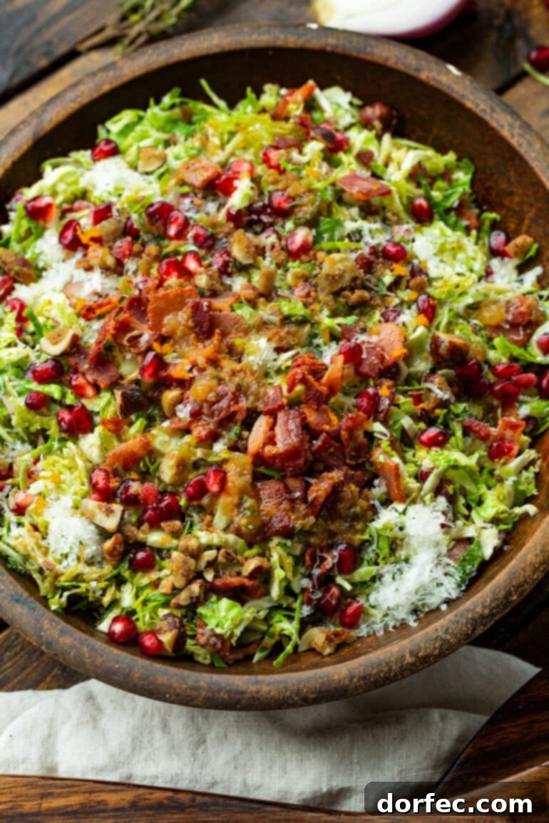 Jewel-Toned Brussels Sprouts with Pomegranate 7 An untossed Brussels sprouts and pomegranate salad, showcasing distinct layers of shaved Brussels sprouts, crispy bacon bits, jewel-like pomegranate arils, and crunchy candied nuts, awaiting the final dressing.