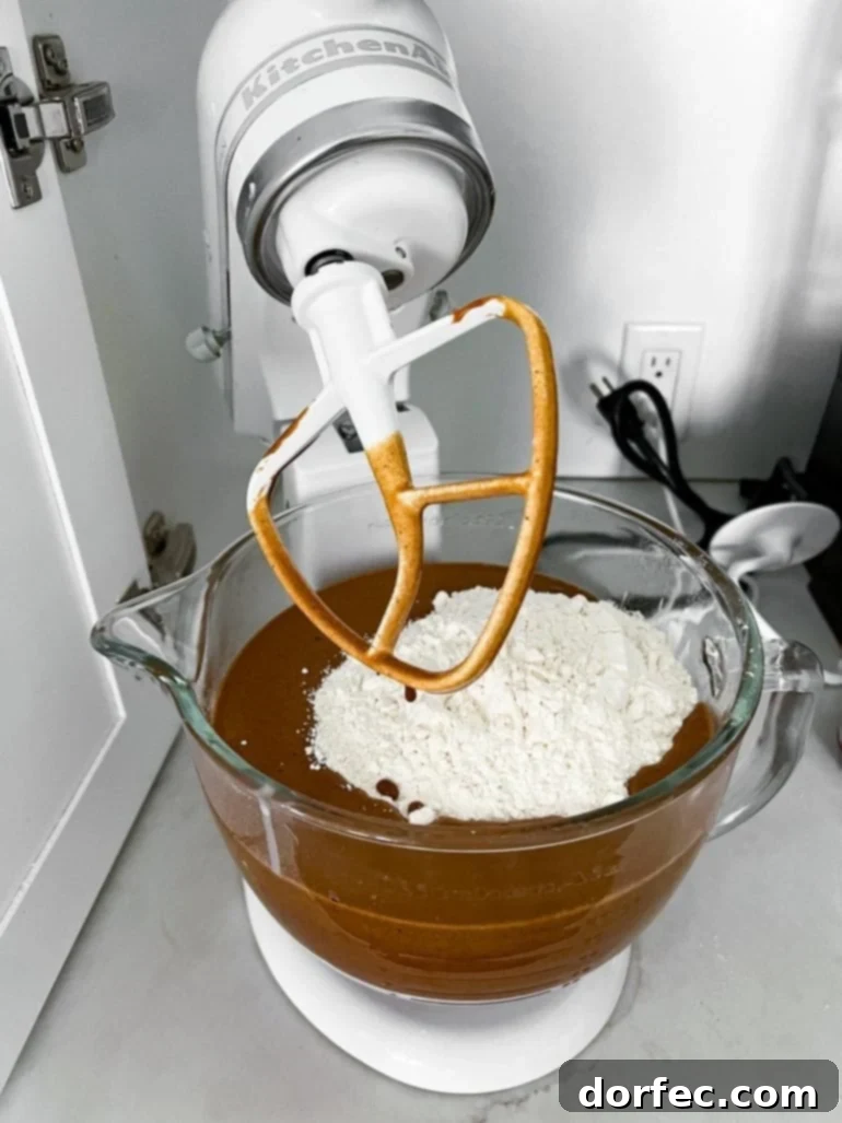 Irresistibly Soft and Chewy Gingerbread Man Cookies for Christmas 2 a photo of gingerbread cookie batter in the glass mixing bowl of a stand mixer with a cup of flour sitting on top ready to mix in.