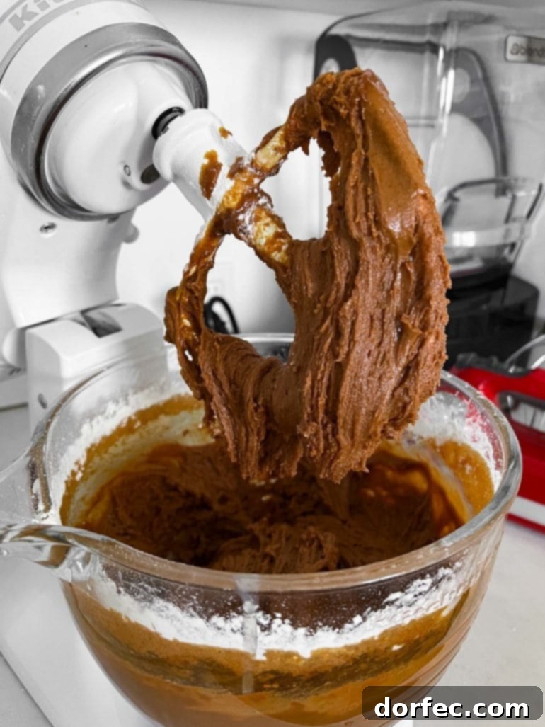 Irresistibly Soft and Chewy Gingerbread Man Cookies for Christmas 3 a photo of the glass bowl of a stand mixer full of gingerbread men cookie dough. the mixing paddle has been lifted so you can see the consistency of the dough falling off the paddle.