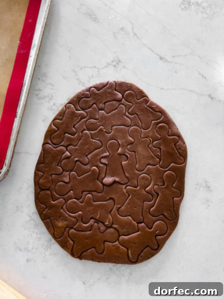 Irresistibly Soft and Chewy Gingerbread Man Cookies for Christmas 4 a photo of gingerbread cookie dough rolled out on the counter top with little gingerbread men cut into the dough all over.