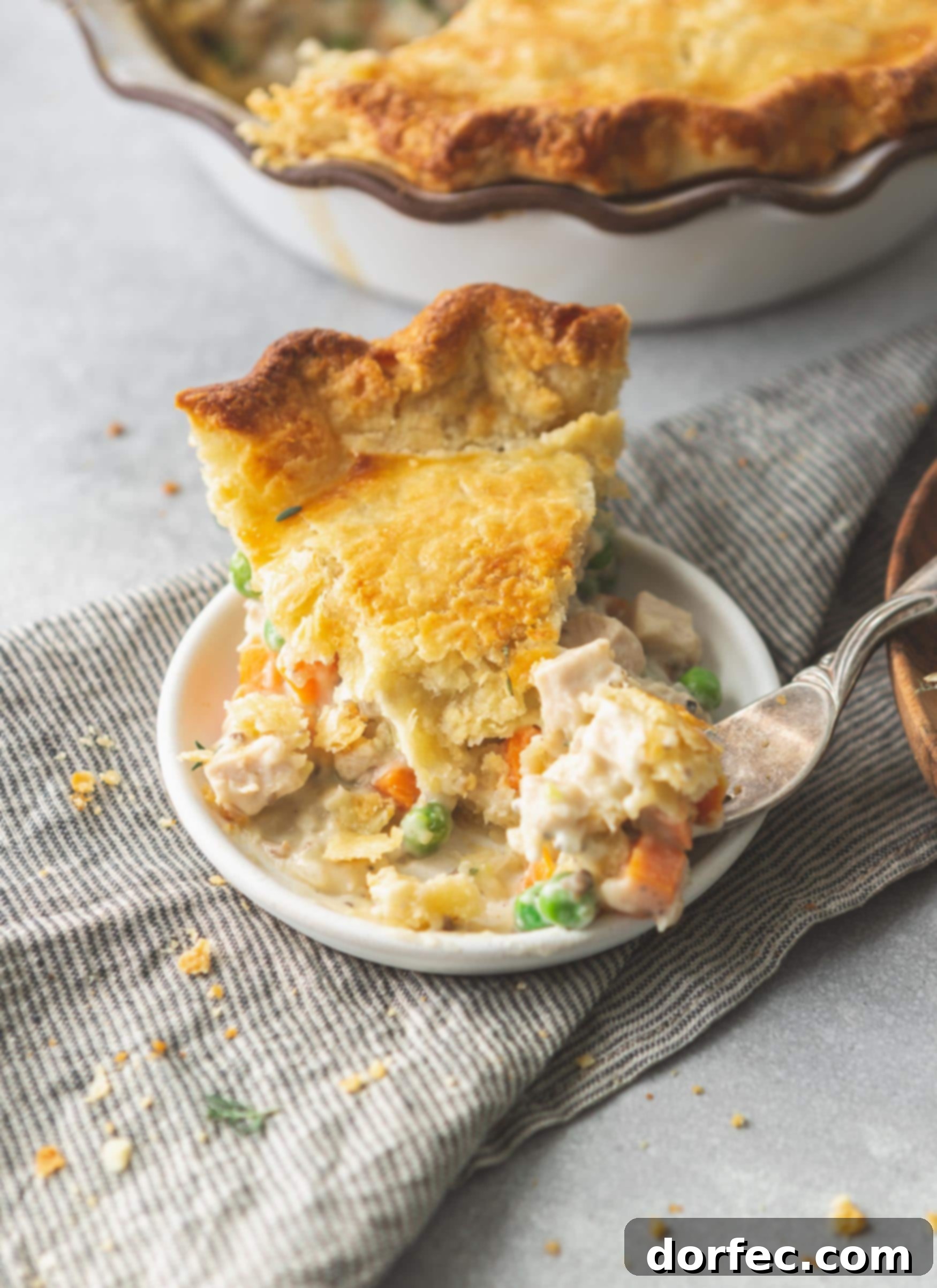 A slice of turkey pot pie on a small plate. The crust is golden brown and the filling is creamy and contains carrots and pies.