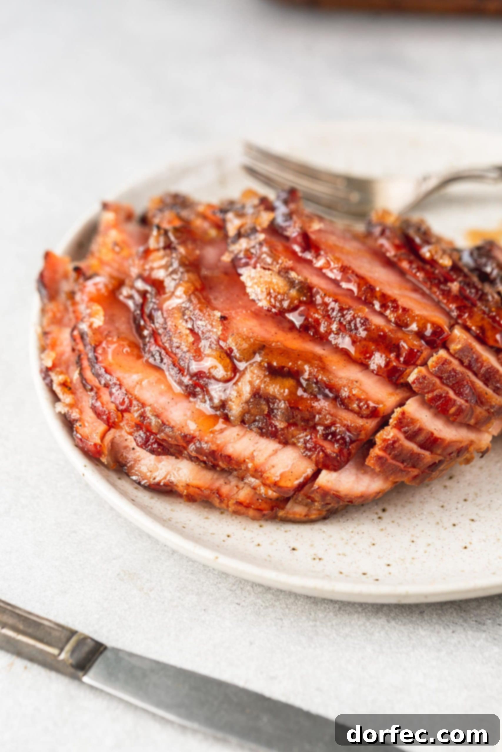 A spiral cut honey glazed ham on a serving plate with a fork next to it. The slices are slightly separated so you can see the juicy meat and honey glaze.