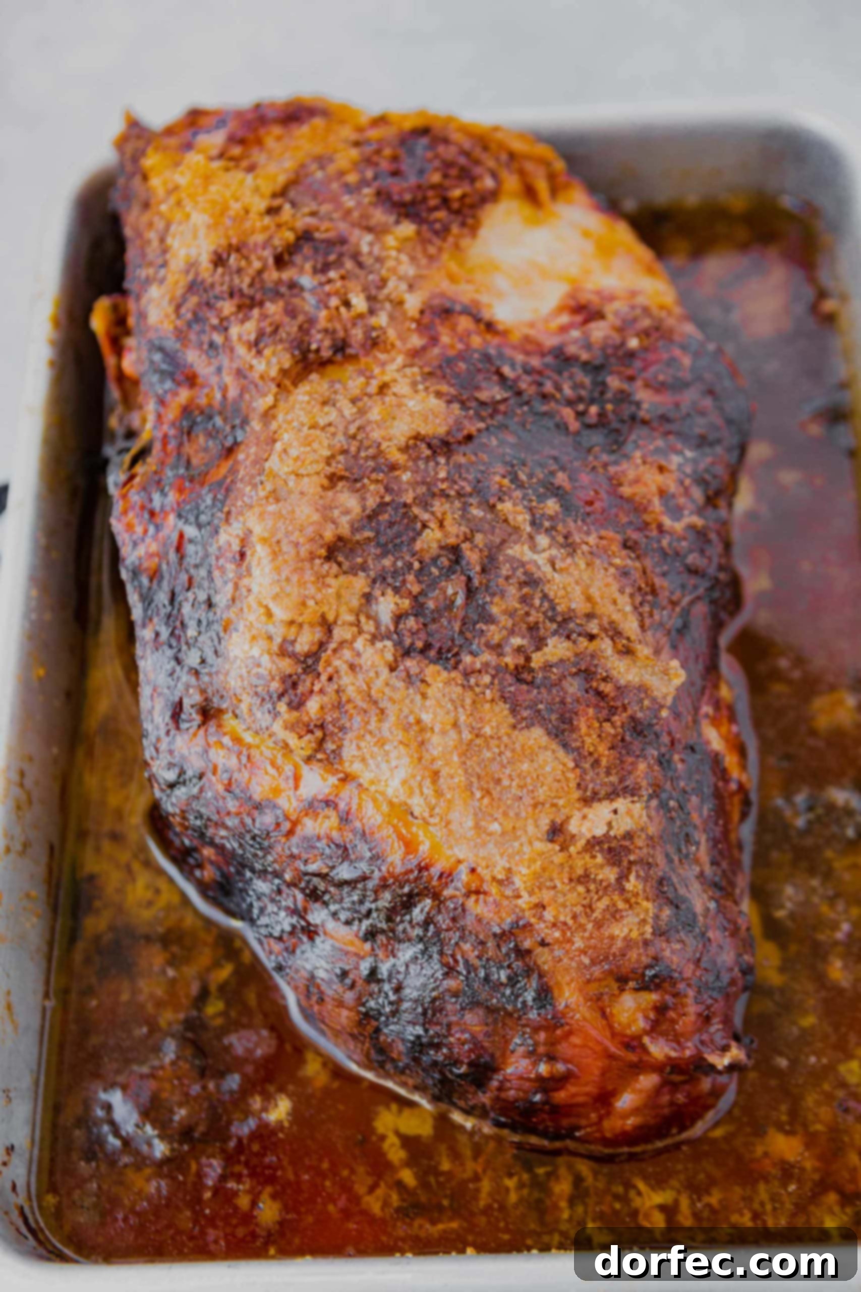 A perfectly roasted whole pork butt in a white baking dish sitting in its juices ready to be shredded.