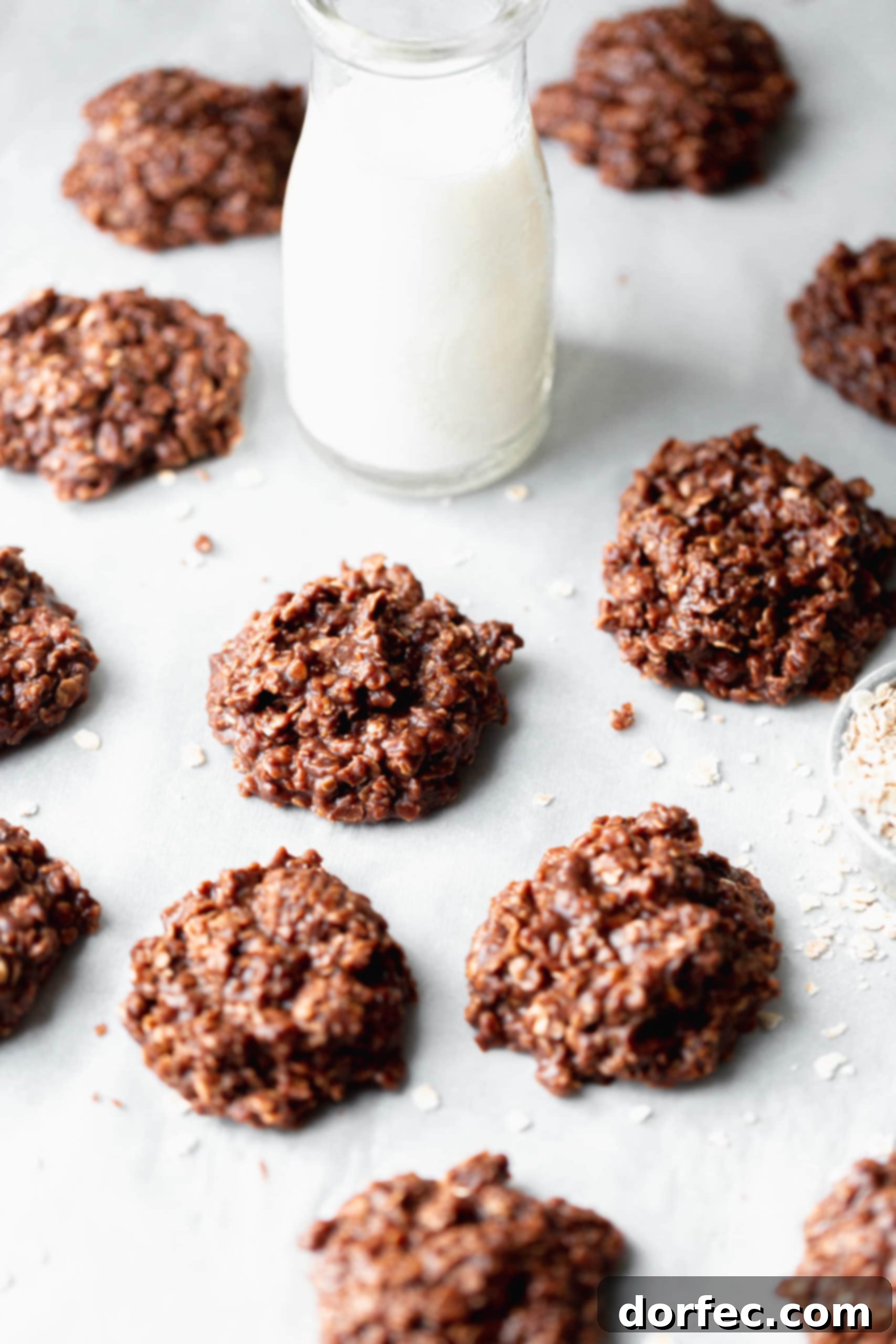 A tantalizing spread of chocolate peanut butter no-bake cookies, flecked with oats, on parchment paper, accompanied by a tall glass of cold milk.