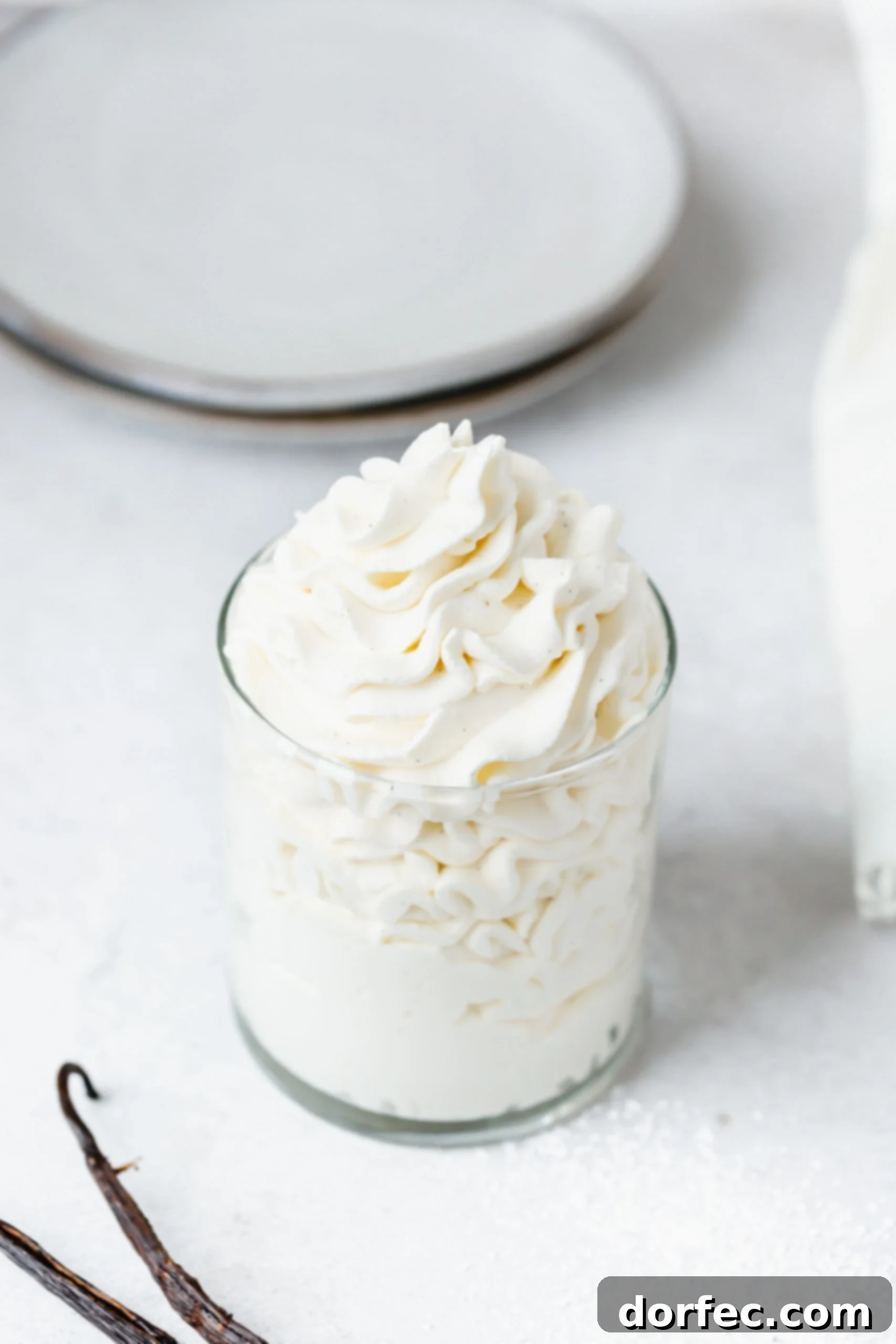 A close-up shot of fluffy vanilla bean whipped cream in a clear glass container, showcasing its smooth texture and subtle vanilla specks.