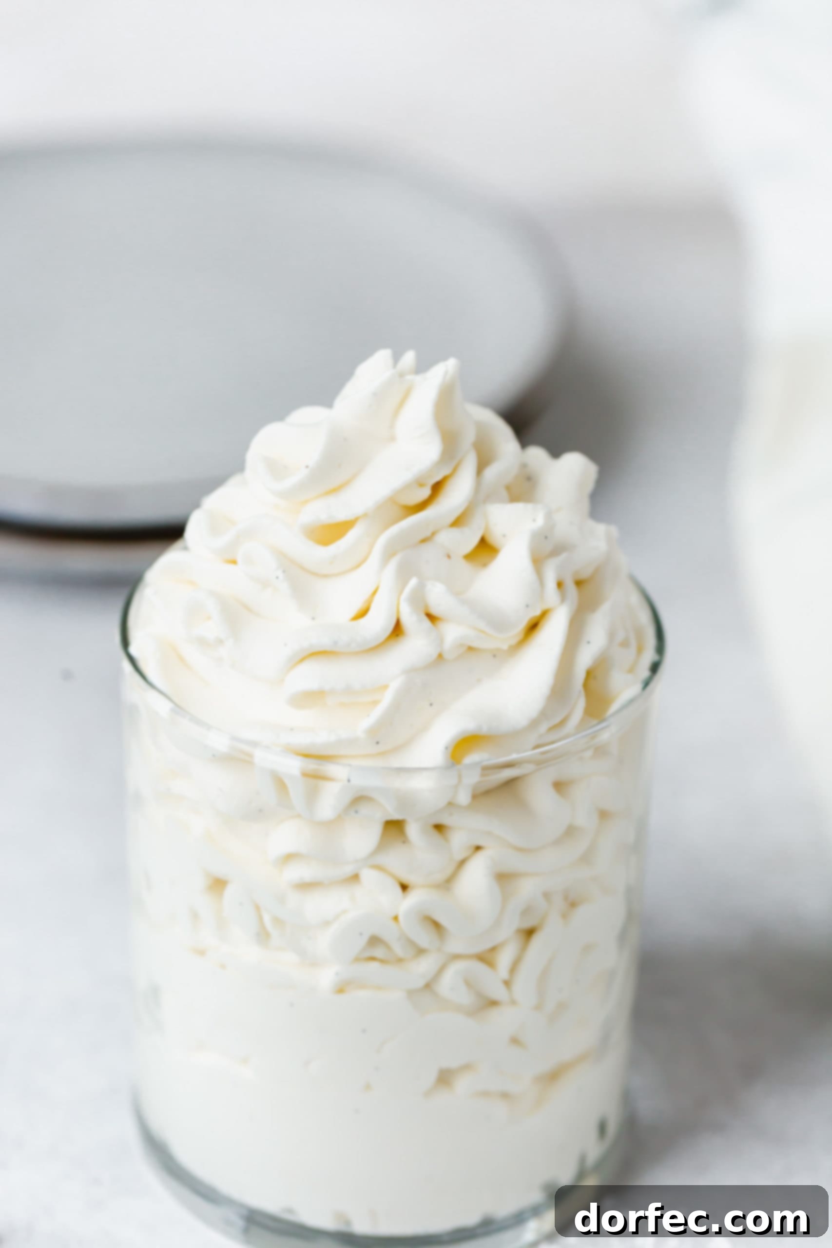 A pristine glass of perfectly whipped vanilla bean cream, fluffy and white, adorned with visible vanilla specks, ready for a dessert.