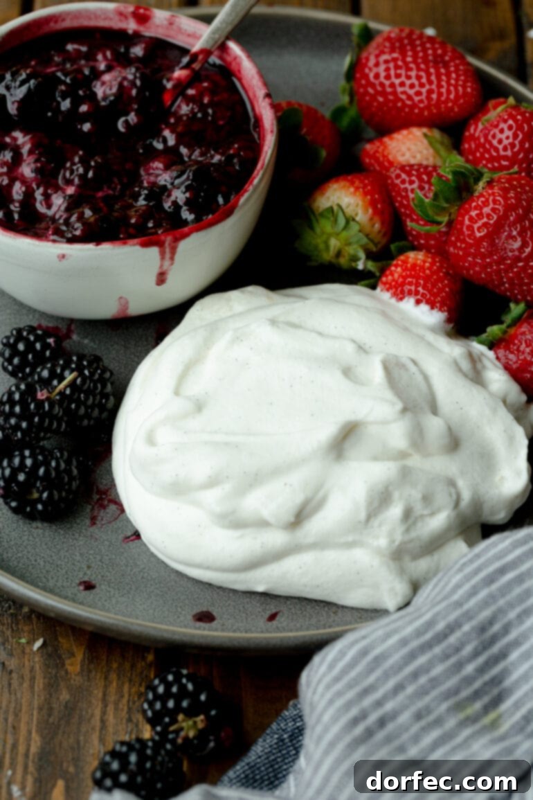 A delectable serving of vanilla bean whipped cream on a plate, elegantly paired with an assortment of fresh berries and a rich berry sauce.