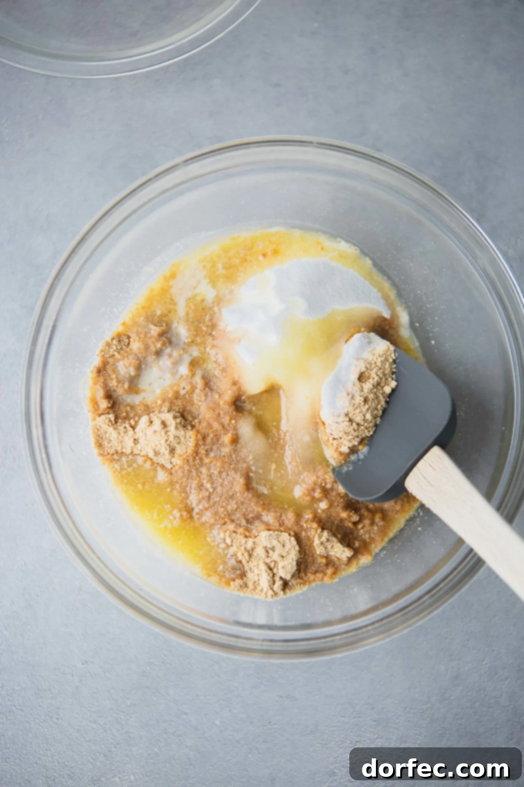 Graham Cracker Crust Graham cracker crumbs, granulated sugar, and melted butter being gently folded together in a clear glass mixing bowl with a rubber spatula, creating the base for a delicious pie crust.