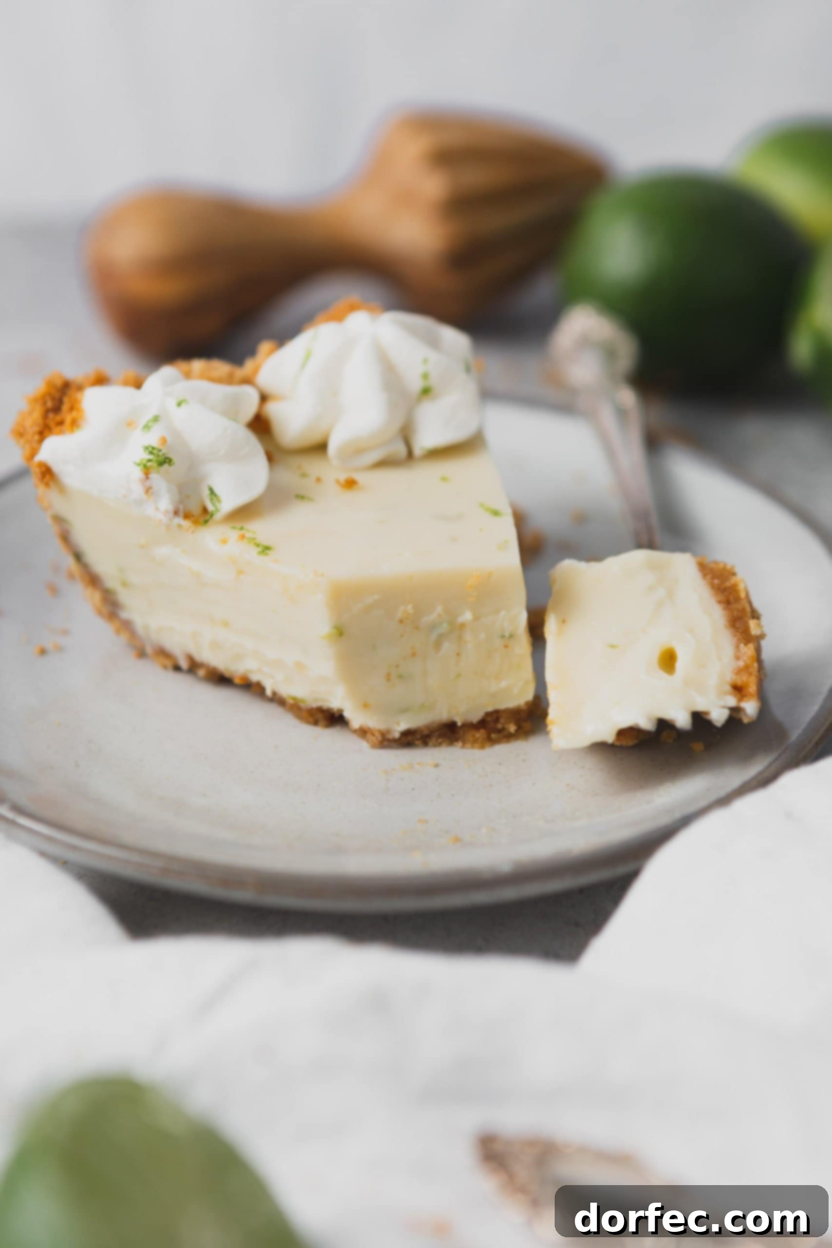 Key Lime Pie with Whipped Cream A close-up of a delightful slice of Key Lime Pie, featuring a fork poised to take a bite. Two dollops of stabilized whipped cream and a sprinkle of fresh lime zest adorn the top, highlighting the pie's creamy texture and vibrant flavor.