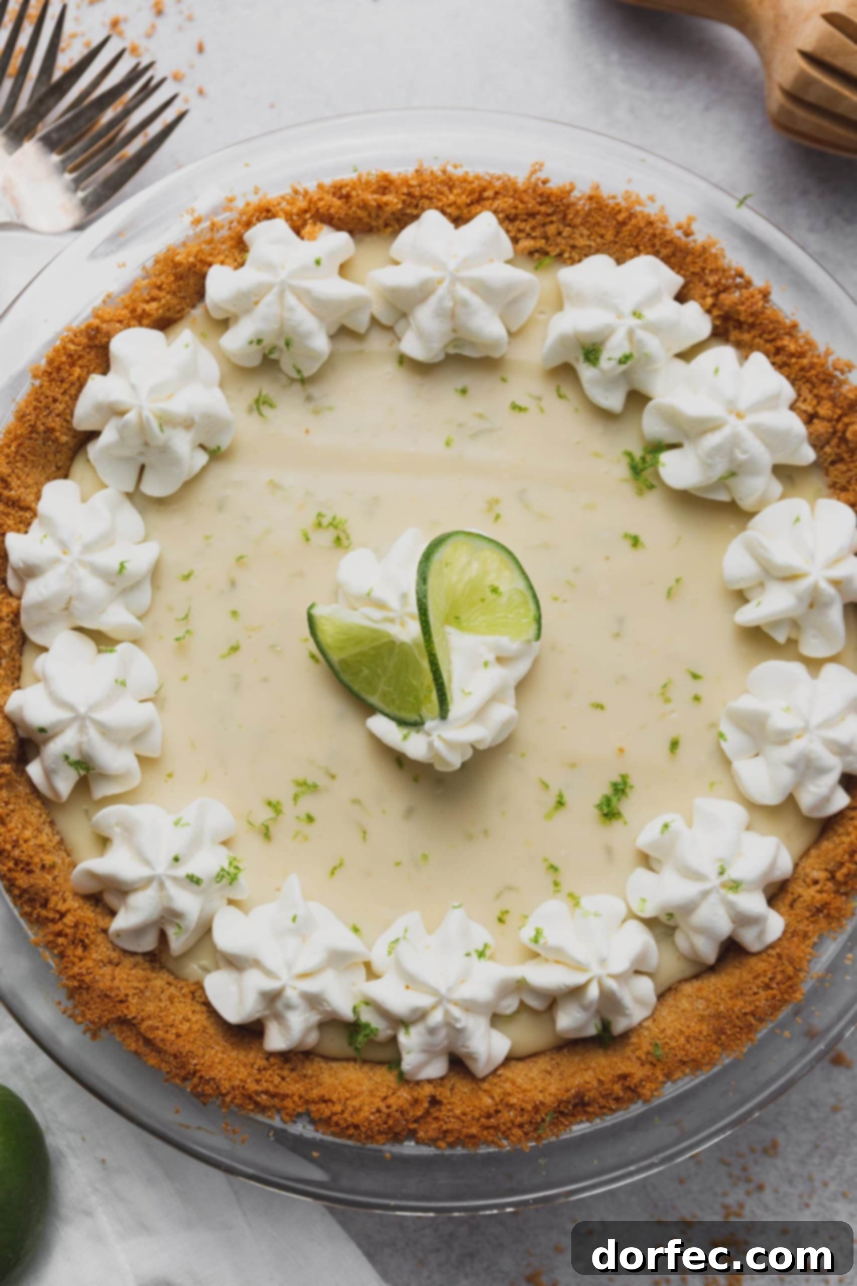 Decorated Key Lime Pie A stunning top-down view of a complete Key Lime Pie, featuring a perfectly golden graham cracker crust. The smooth, creamy filling is artfully topped with delicate specks of fresh lime zest, elegant dollops of whipped cream, and a decorative curl of lime peel.