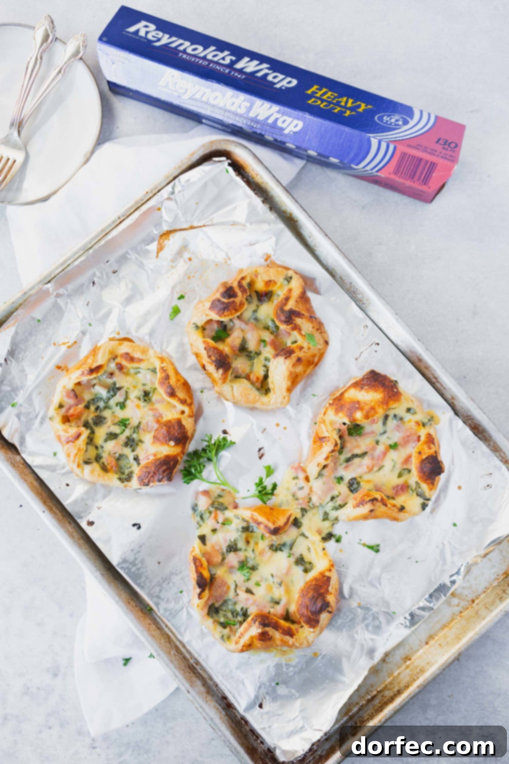 Four perfectly golden ham and cheese puffs resting on a Reynolds Wrap foil-lined baking sheet, with a box of foil nearby, emphasizing easy baking and cleanup.