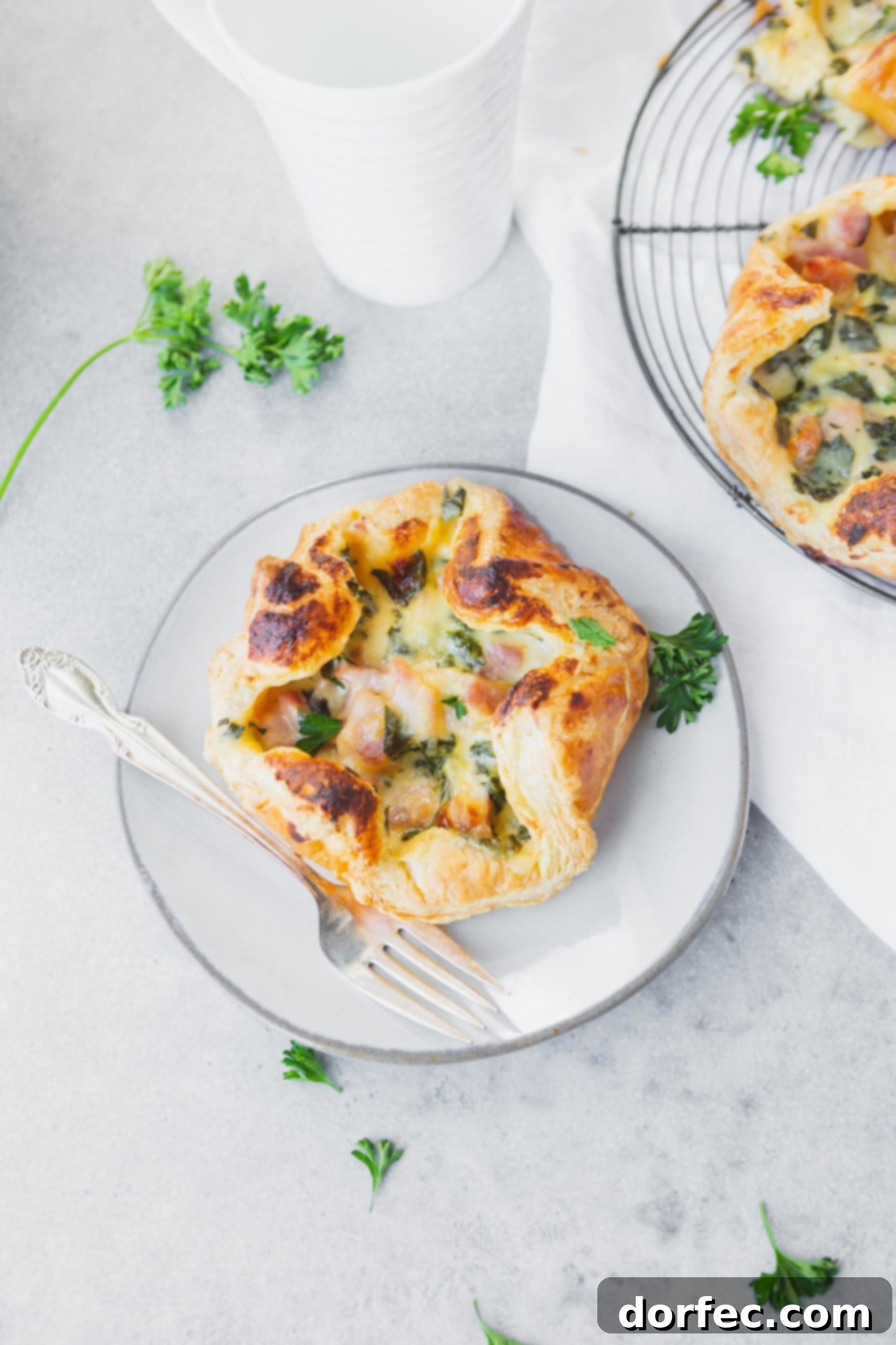 A single golden ham and cheese puff on a white plate, ready to be enjoyed with a silver fork beside it, perfect for brunch or a savory snack.