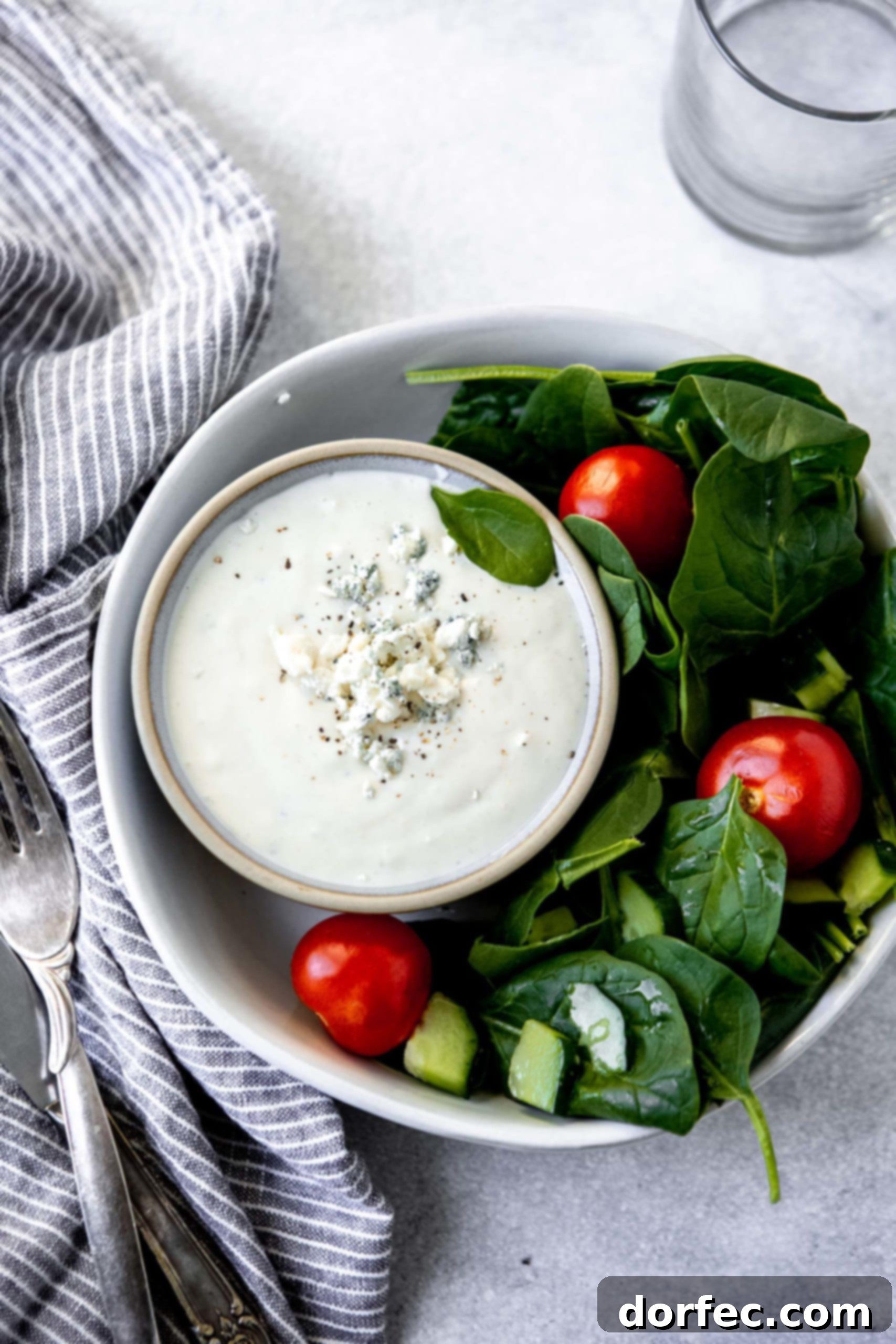 A fresh green salad in a white bowl, accompanied by a small cup of homemade blue cheese dressing.
