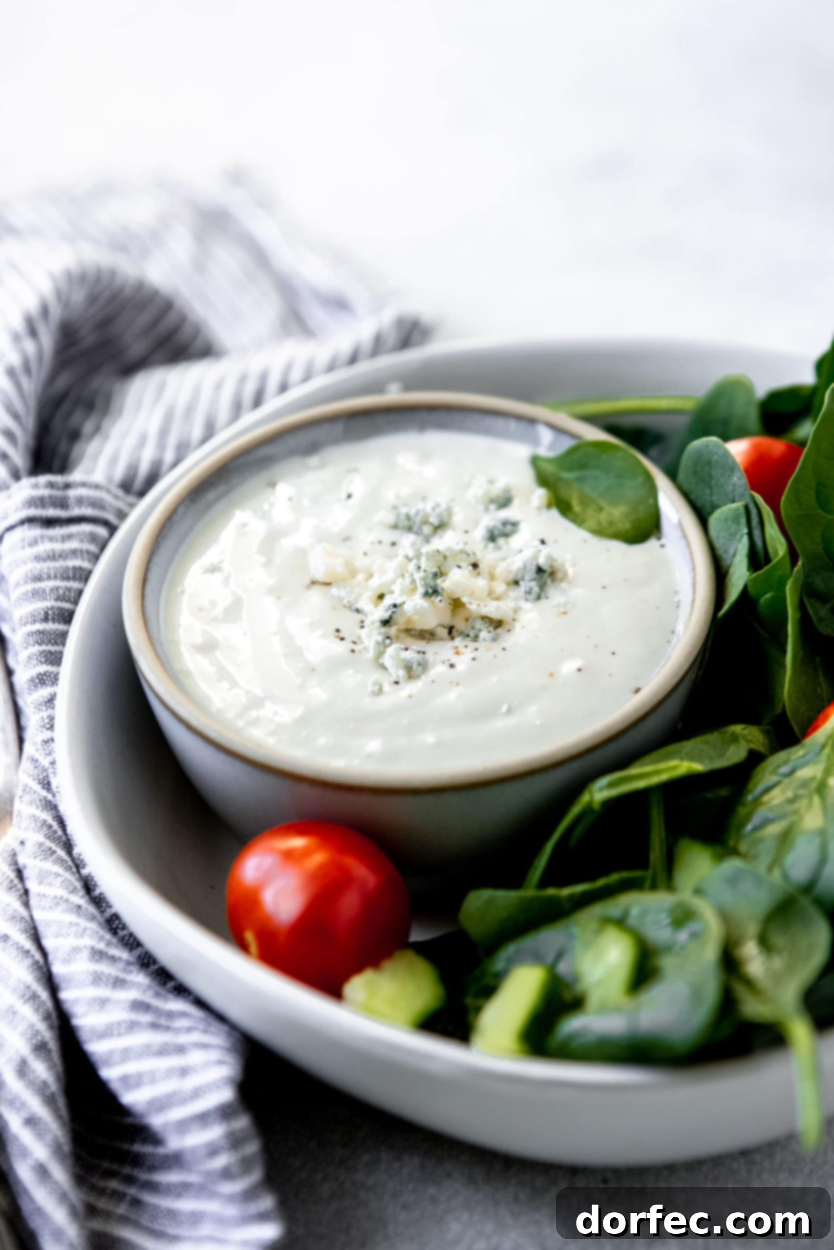 A vibrant green salad served in a white bowl, featuring a small cup of homemade blue cheese dressing nestled within.
