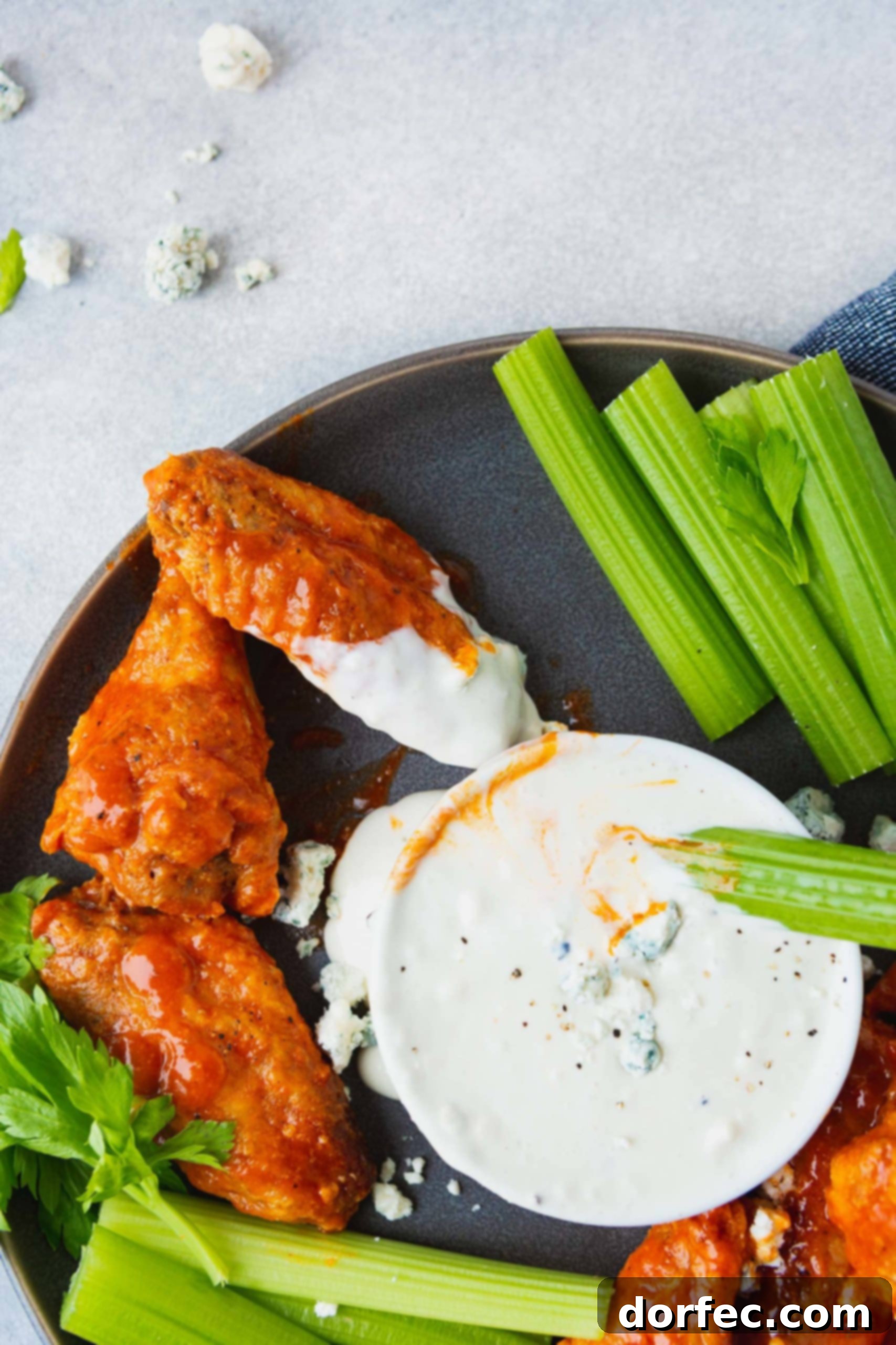 A delicious charcoal platter showcasing buffalo wings and crisp celery, with a bowl of blue cheese dressing at the center. A wing and celery stick are already dipped.