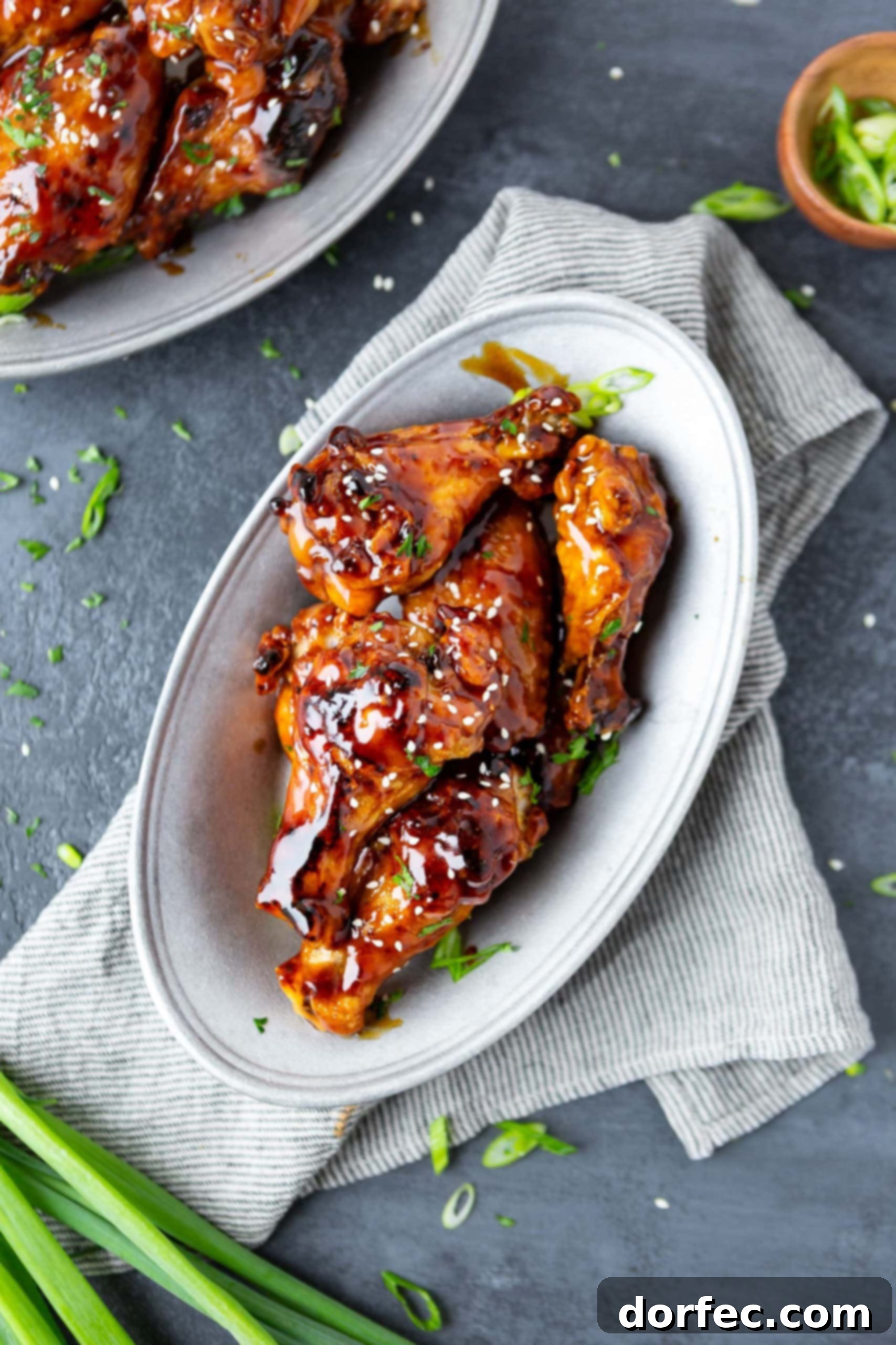 Air Fryer Teriyaki Chicken Wings a photo taken from above of several baked chicken wings coated in teriyaki sauce and topped with sprinkled sesame seeds on a large white platter