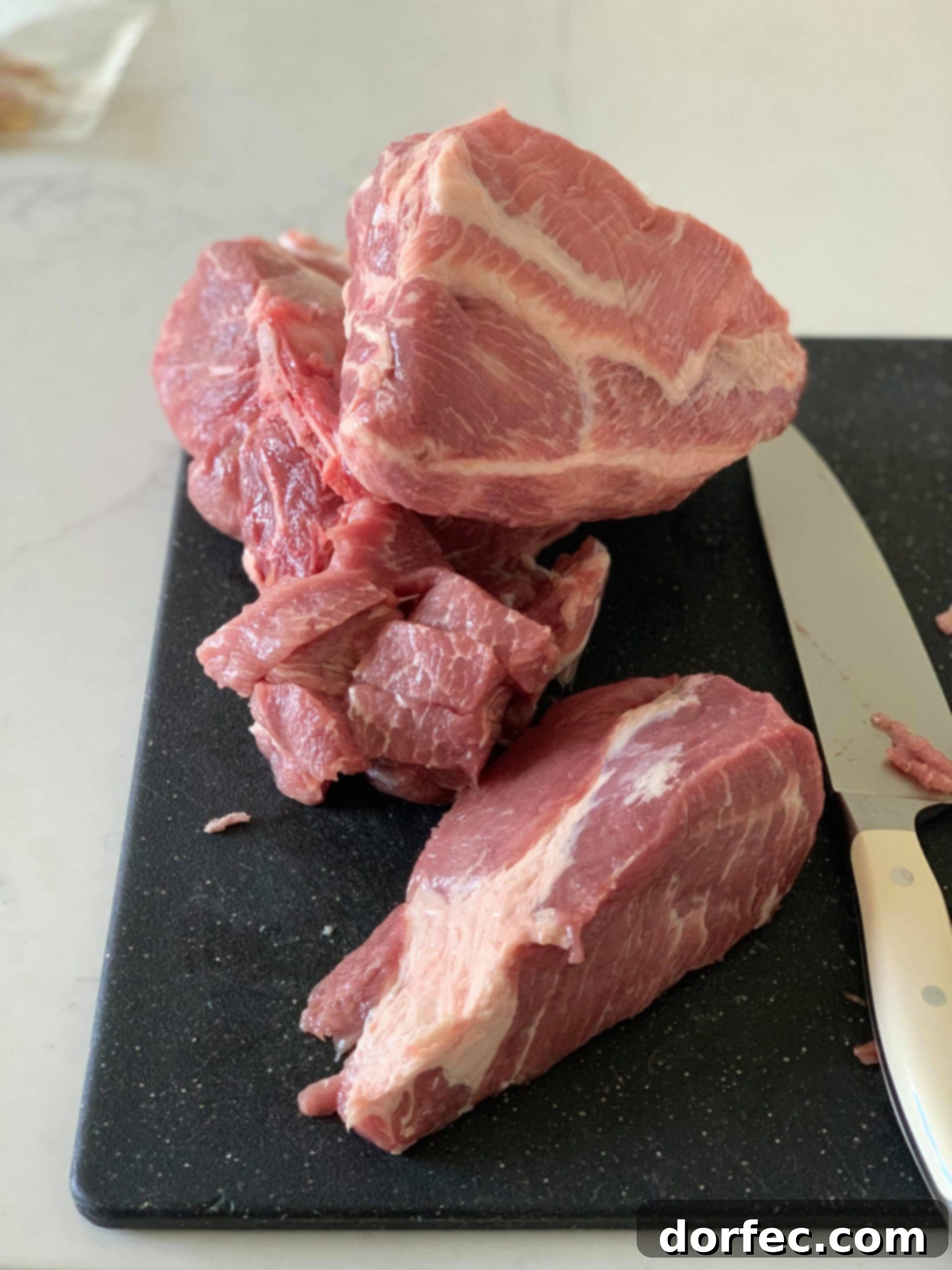 a photo of a raw pork butt cut into three large sections with one of the sections being cut into 2" chunks.