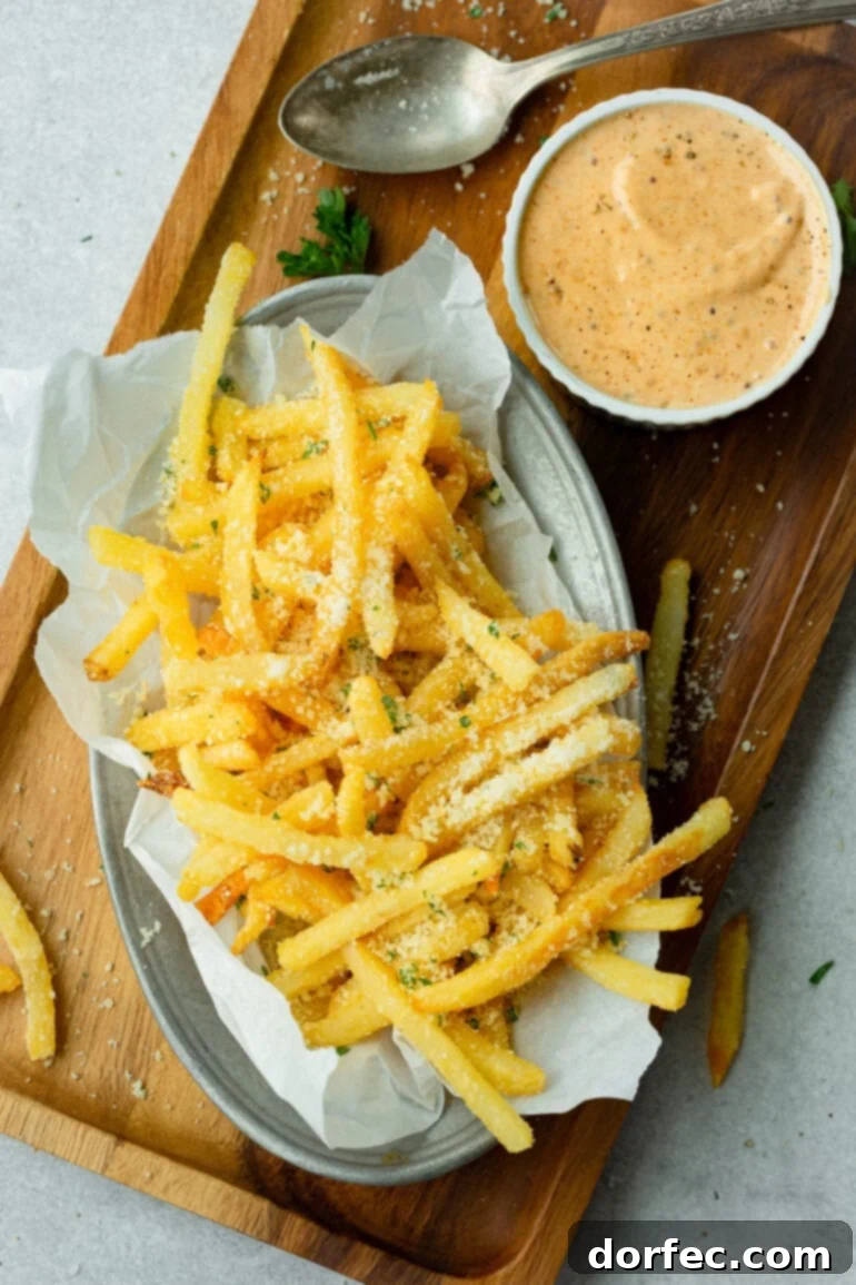 A dish full of hot, salty parmesan fries with a side of creamy Cajun remoulade dipping sauce, inviting a delicious pairing.