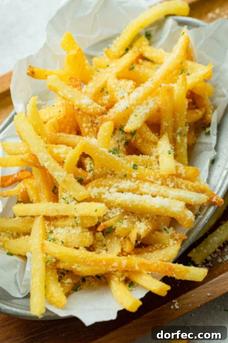 A vibrant photo of a pile of golden, hot, and salty pomme frites generously topped with grated Parmesan cheese, glistening with flavor.