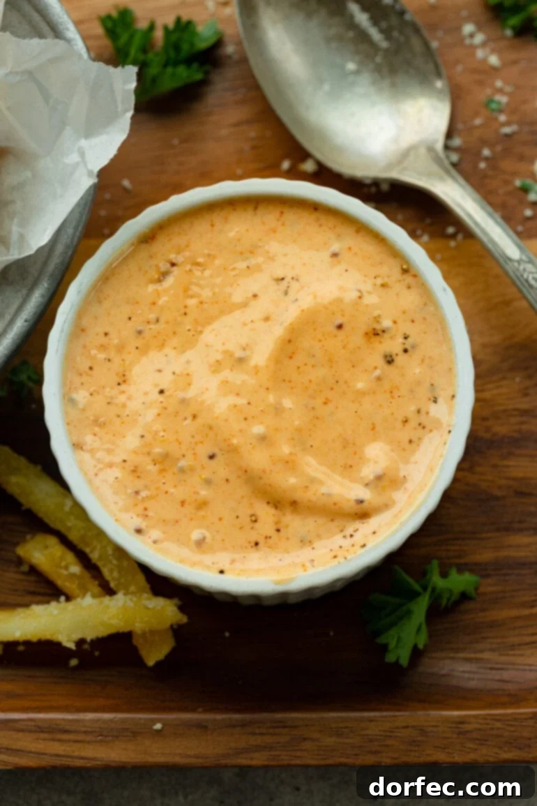 A close-up photo of a small ramekin bowl filled with a rich, creamy Cajun dipping sauce, ready to accompany a batch of delicious french fries.