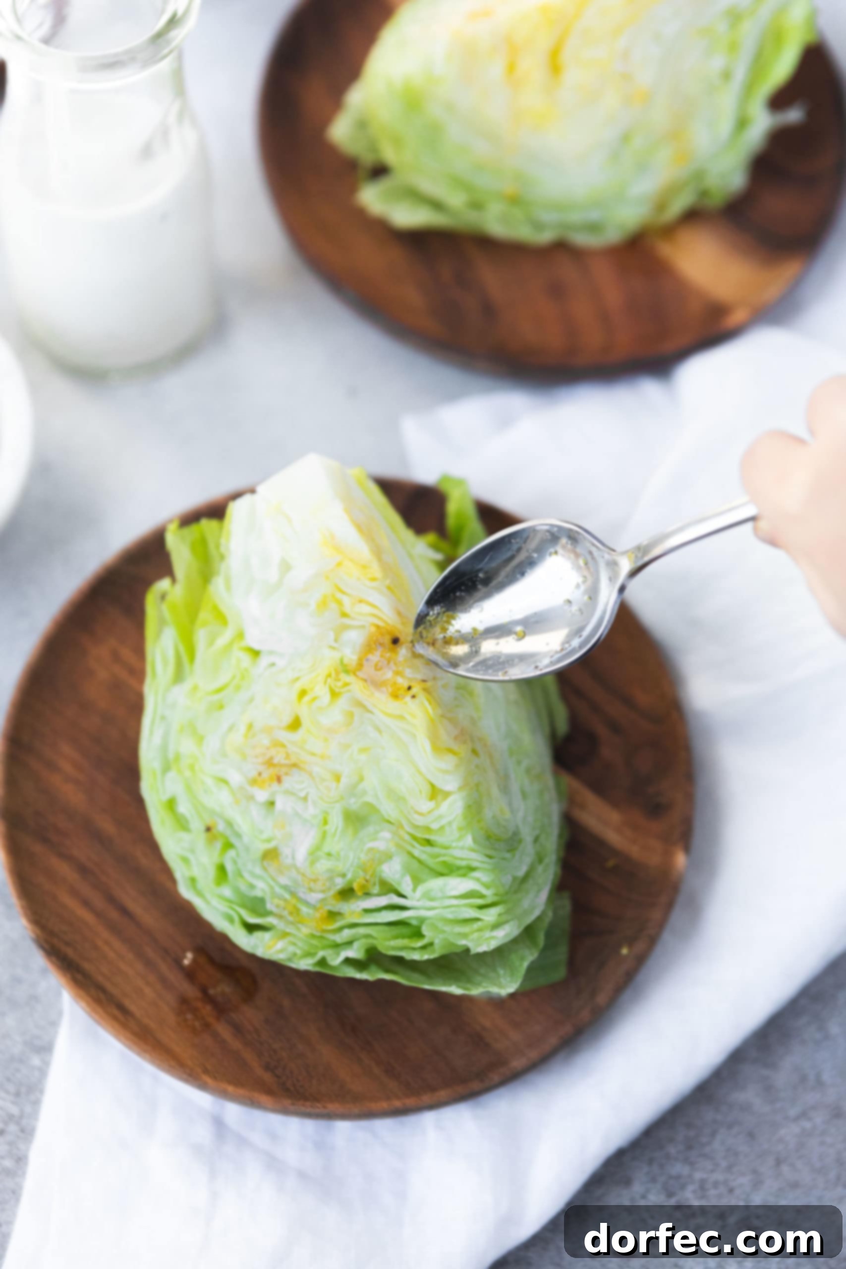 a photo of a wedge of iceberg lettuce being drizzled with a bacon lemon drizzle from a silver spoon.