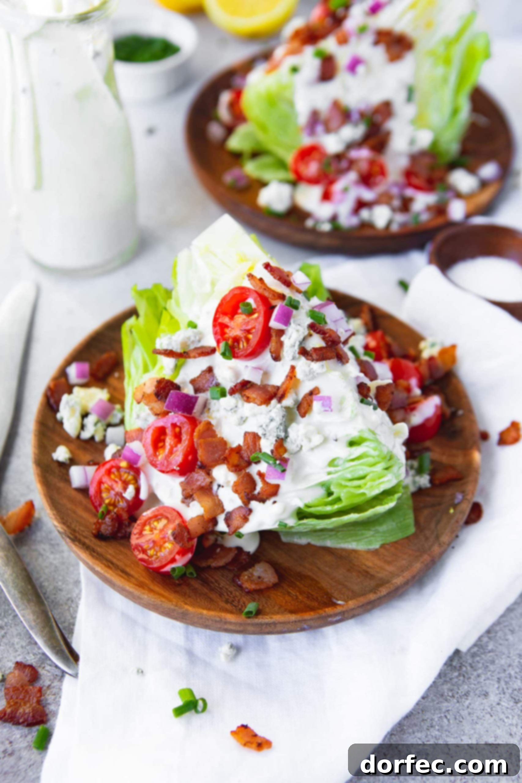 a photo of a wedge salad topped with creamy blue cheese dressing, bacon crumbles, chopped chives and red onions, cherry tomatoes and blue cheese crumbles.