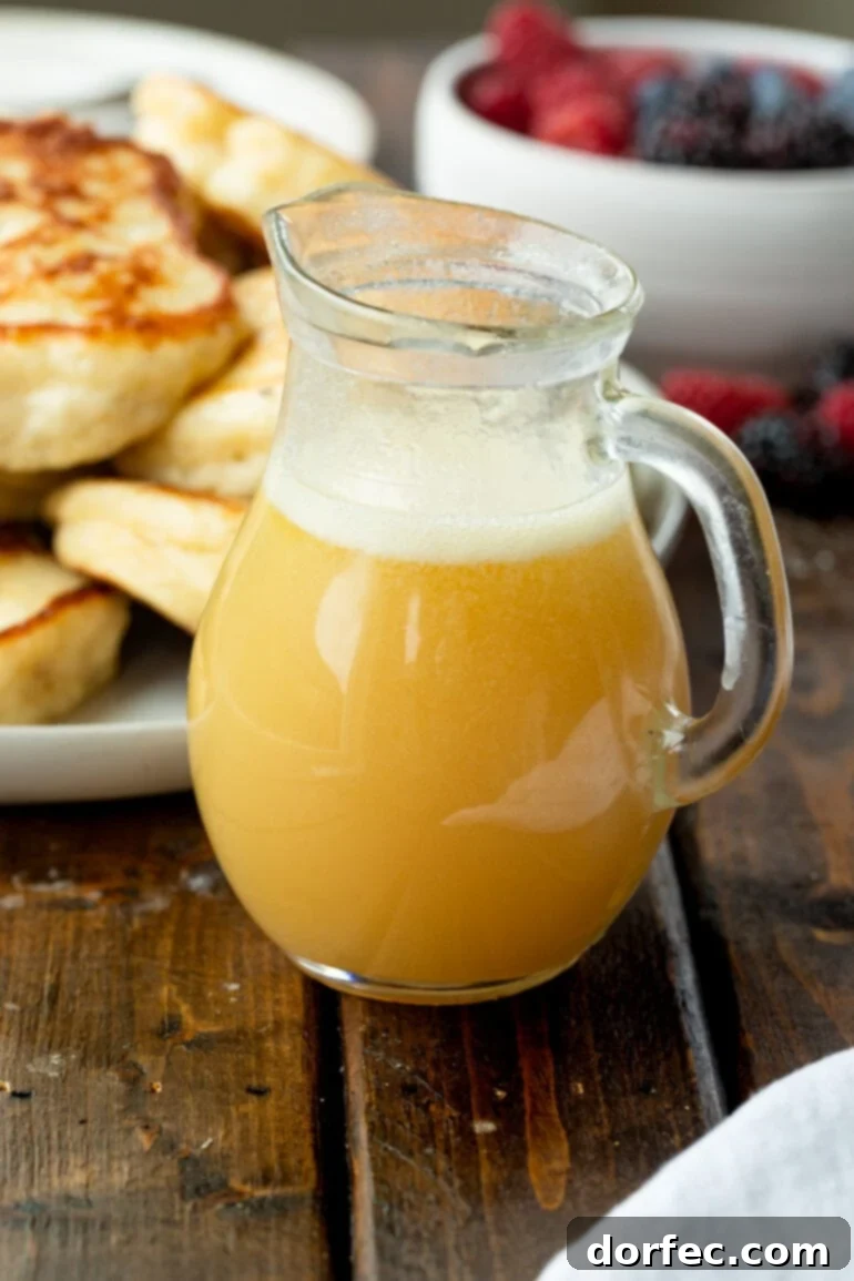 Irresistible Buttermilk Syrup 2 A small glass pitcher full of golden buttermilk syrup, with a stack of golden brown pancakes blurred in the background, ready for a delicious breakfast.
