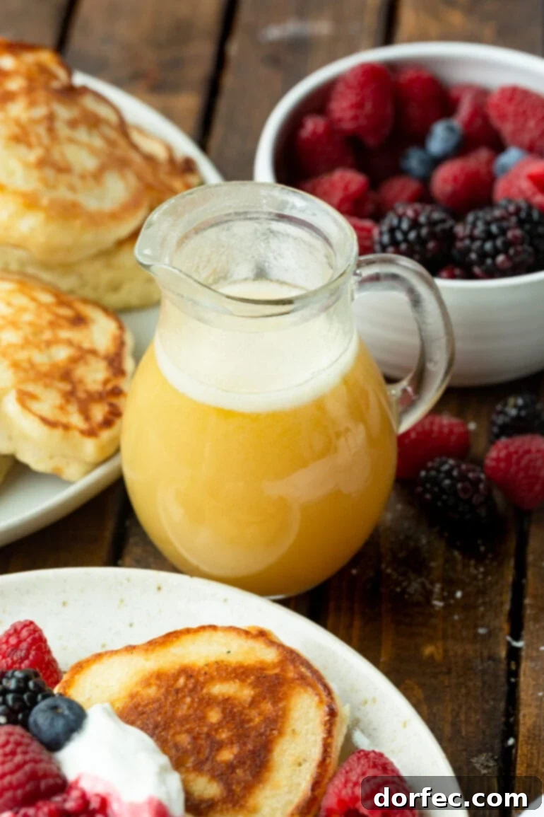 Irresistible Buttermilk Syrup 5 A small glass pitcher of golden buttermilk syrup, with a bowl of fresh mixed berries and a plate of fluffy pancakes creating a perfect breakfast scene.