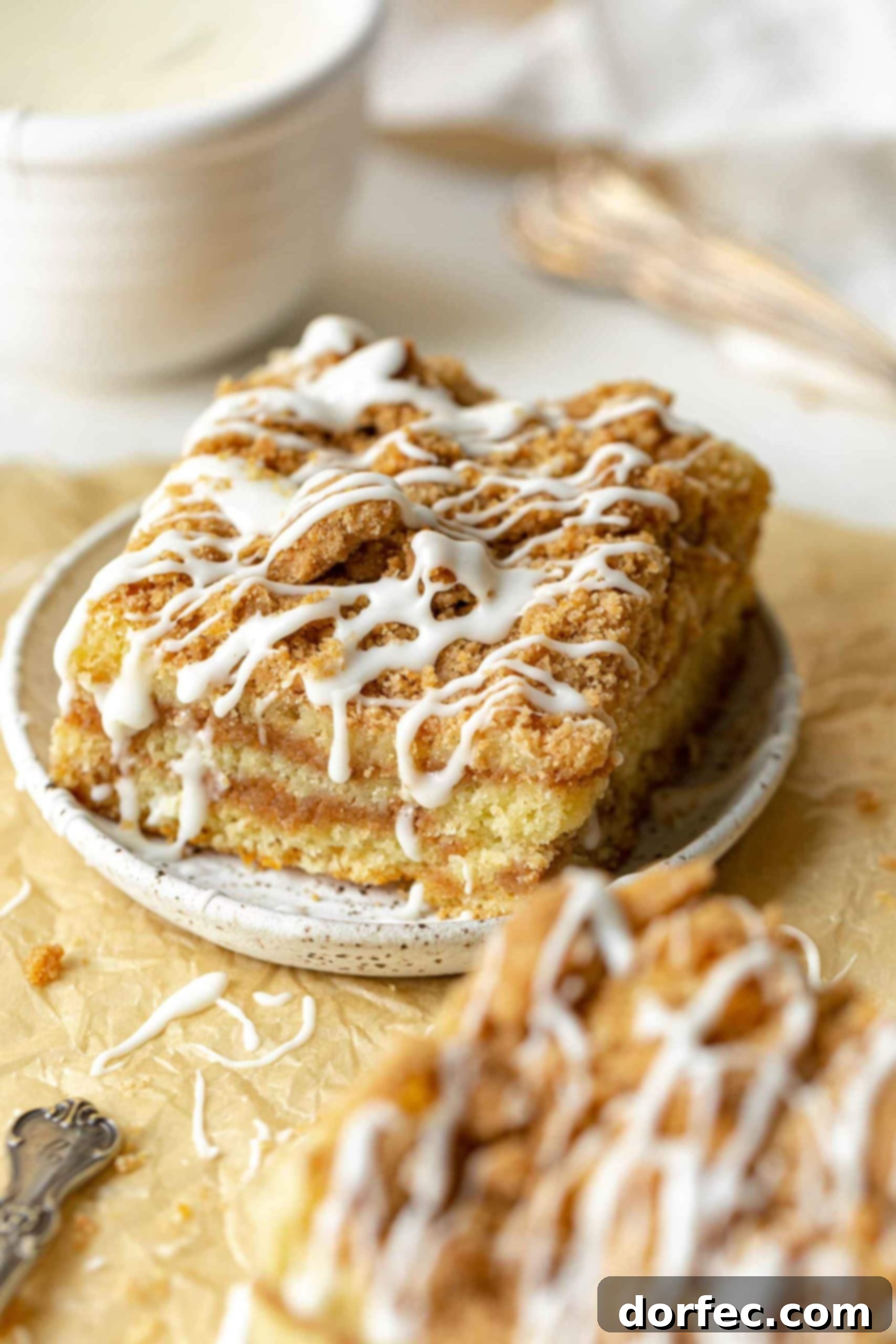 a photo of a piece of coffee cake topped with icing drizzles on a small saucer with another piece in the foreground.