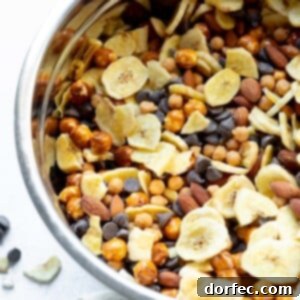 A large metal mixing bowl full of banana chips trail mix with caramel bits, pretzel rounds, almonds and dark chocolate chips, ready to be served and enjoyed.