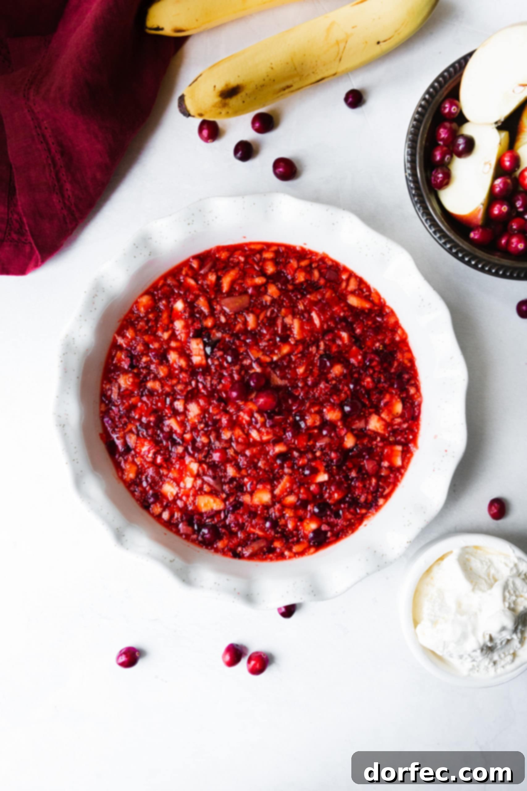 A beautiful white ceramic pie dish brimming with vibrant Christmas Cranberry Jell-O, adorned with fresh cranberries scattered around the edge.